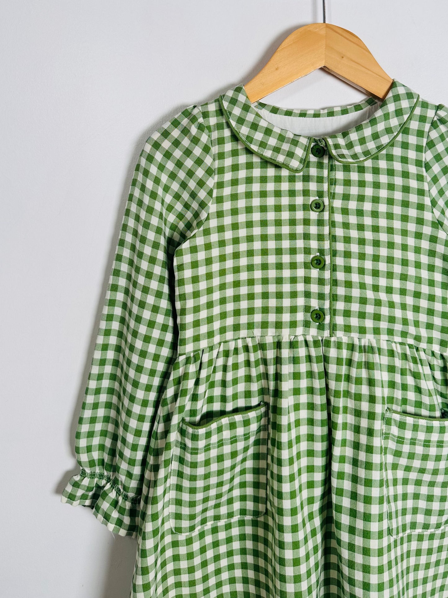 Green and white checkered dress on a wooden hanger against a light gray background