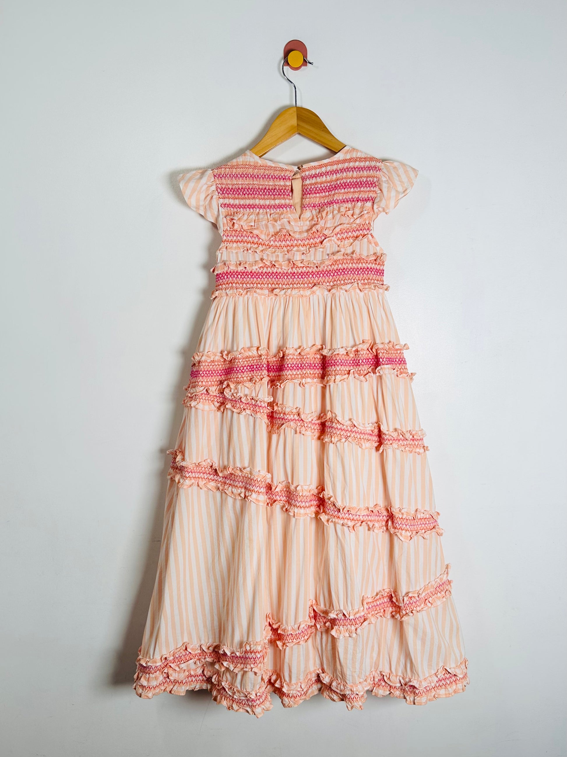 Beige and pink dress with ruffled details on a hanger against a white background