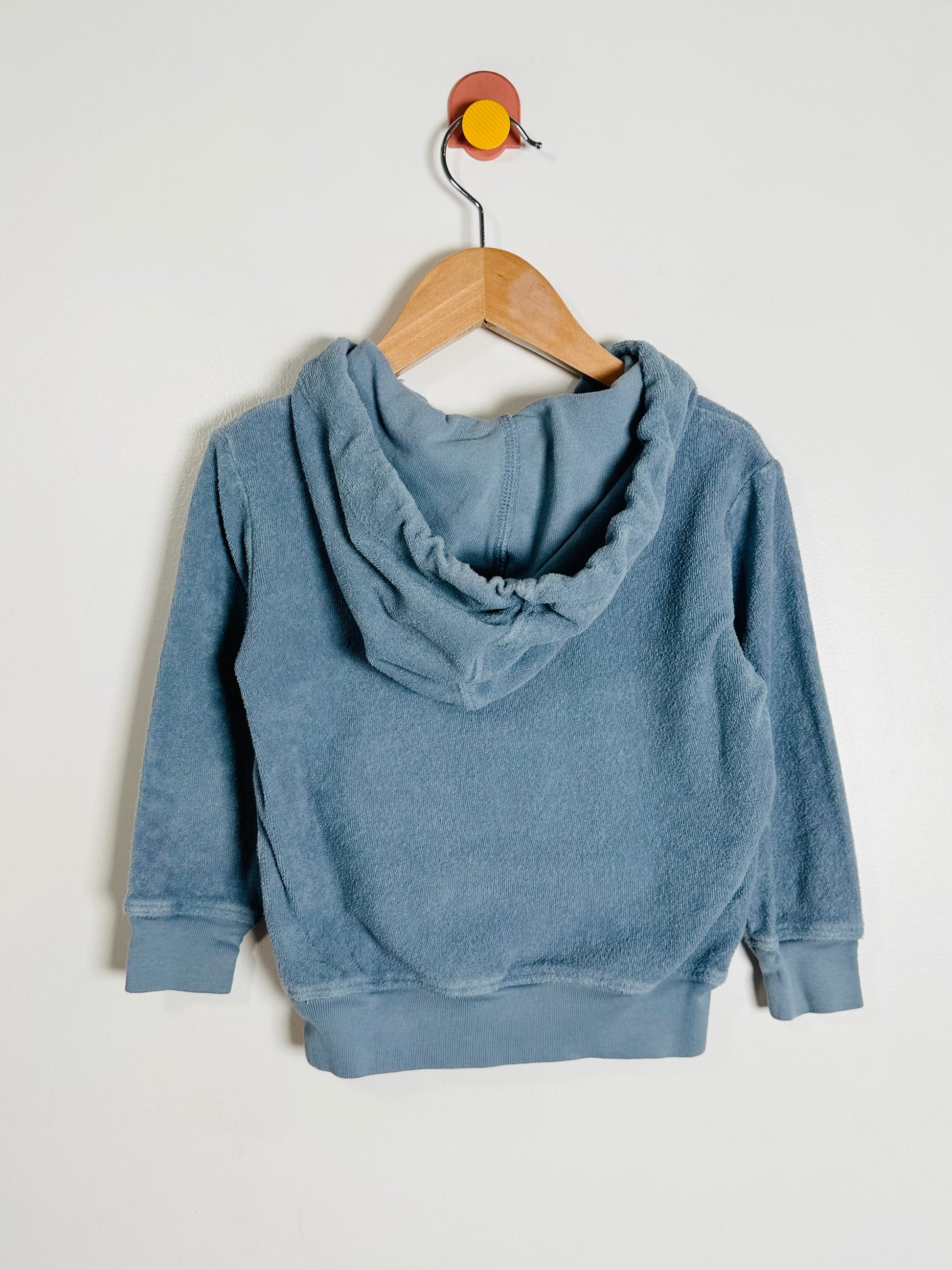 Blue hoodie on a wooden hanger against a light gray background
