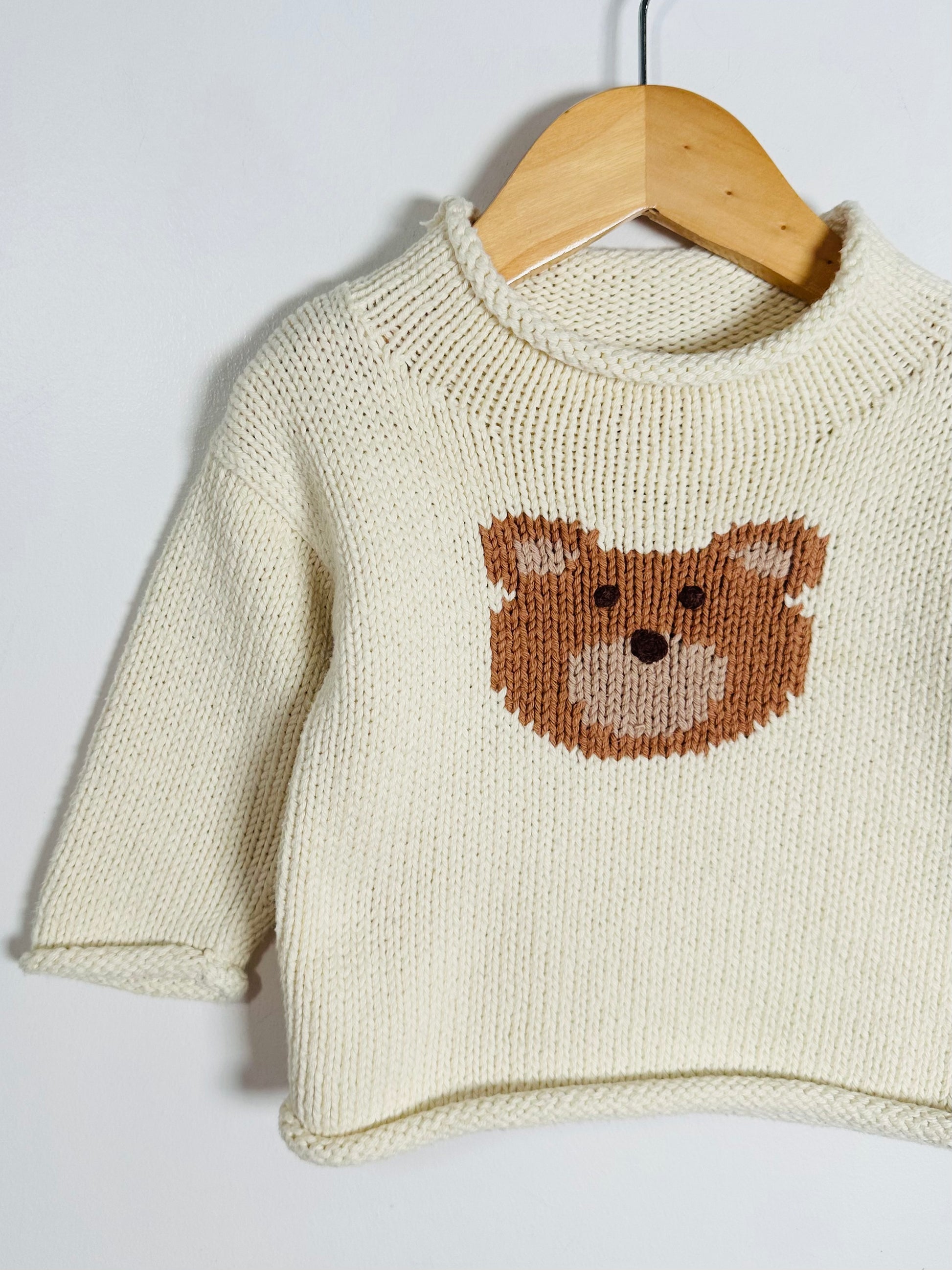 Knitted sweater with a bear face design on a wooden hanger against a white background