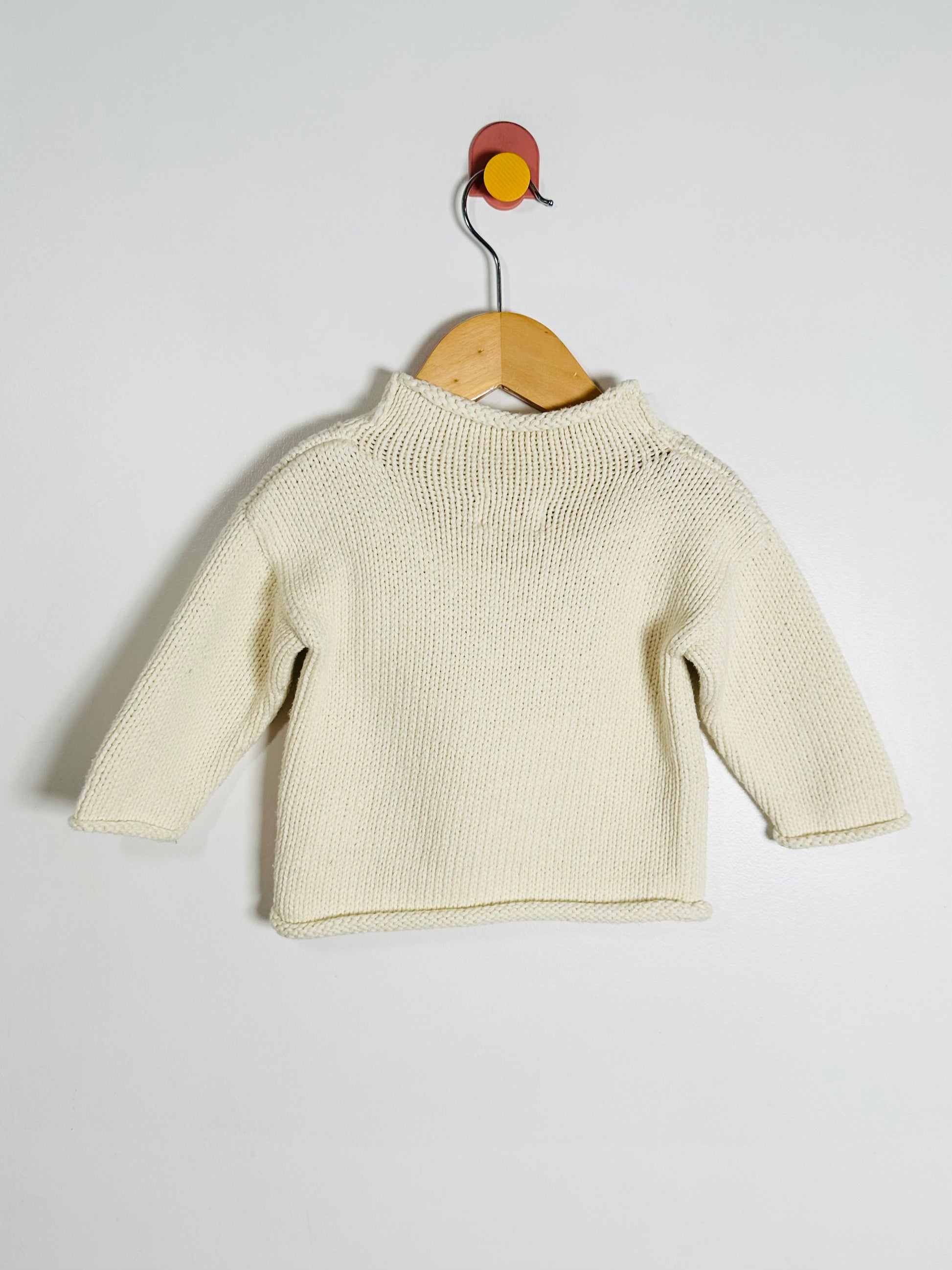 Beige baby sweater on a wooden hanger against a white background