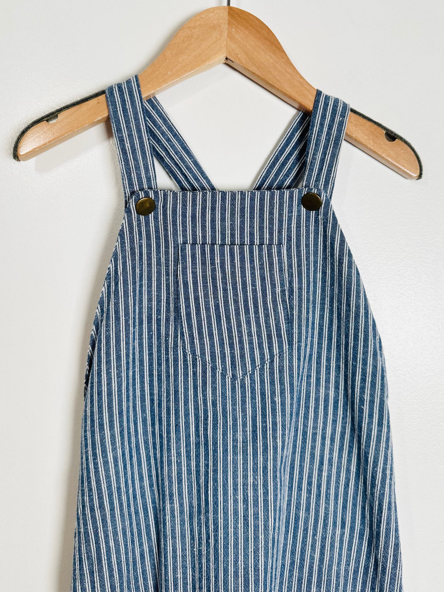 Blue and white striped overalls hanging on a wooden hanger against a white background