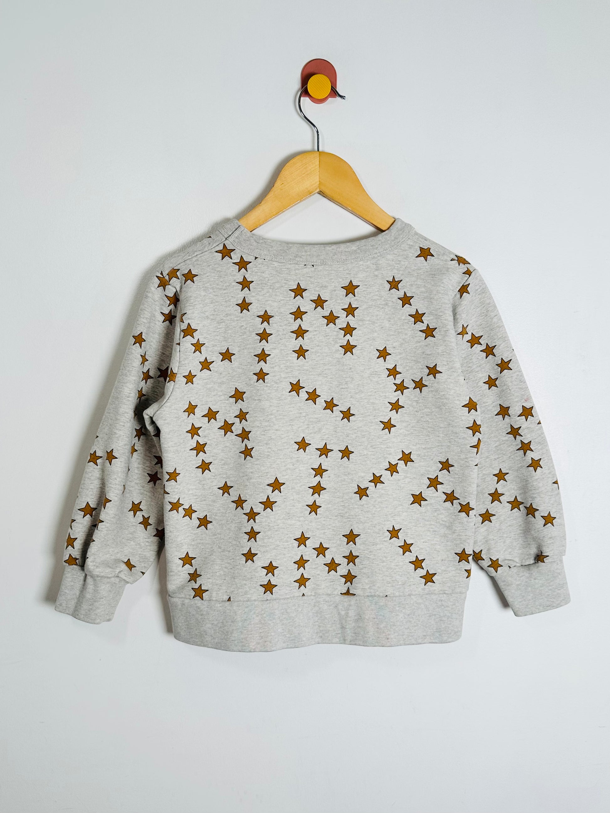 Gray sweatshirt with star pattern on a wooden hanger against a white background