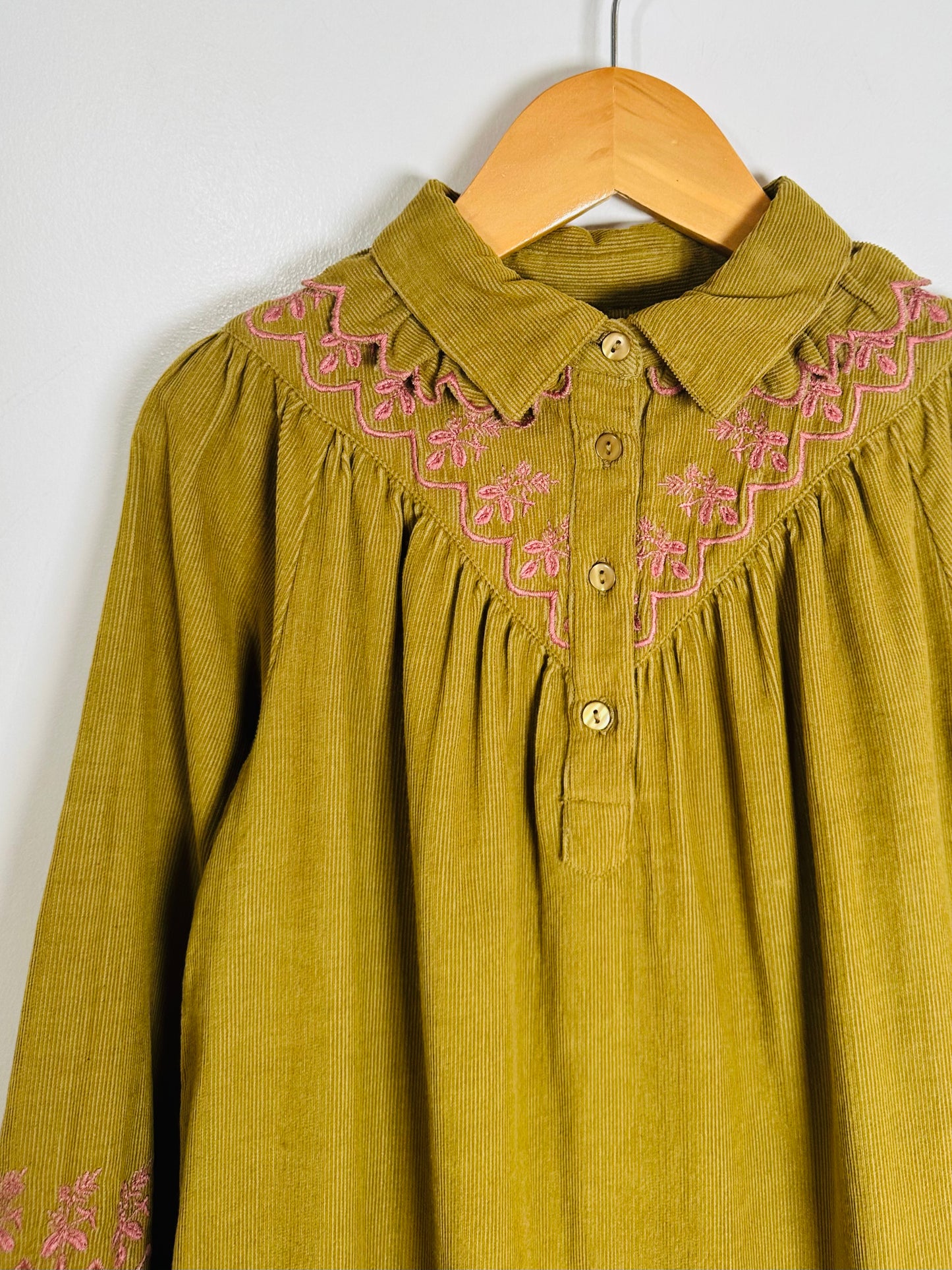 Green corduroy shirt with pink embroidery on a hanger against a white background
