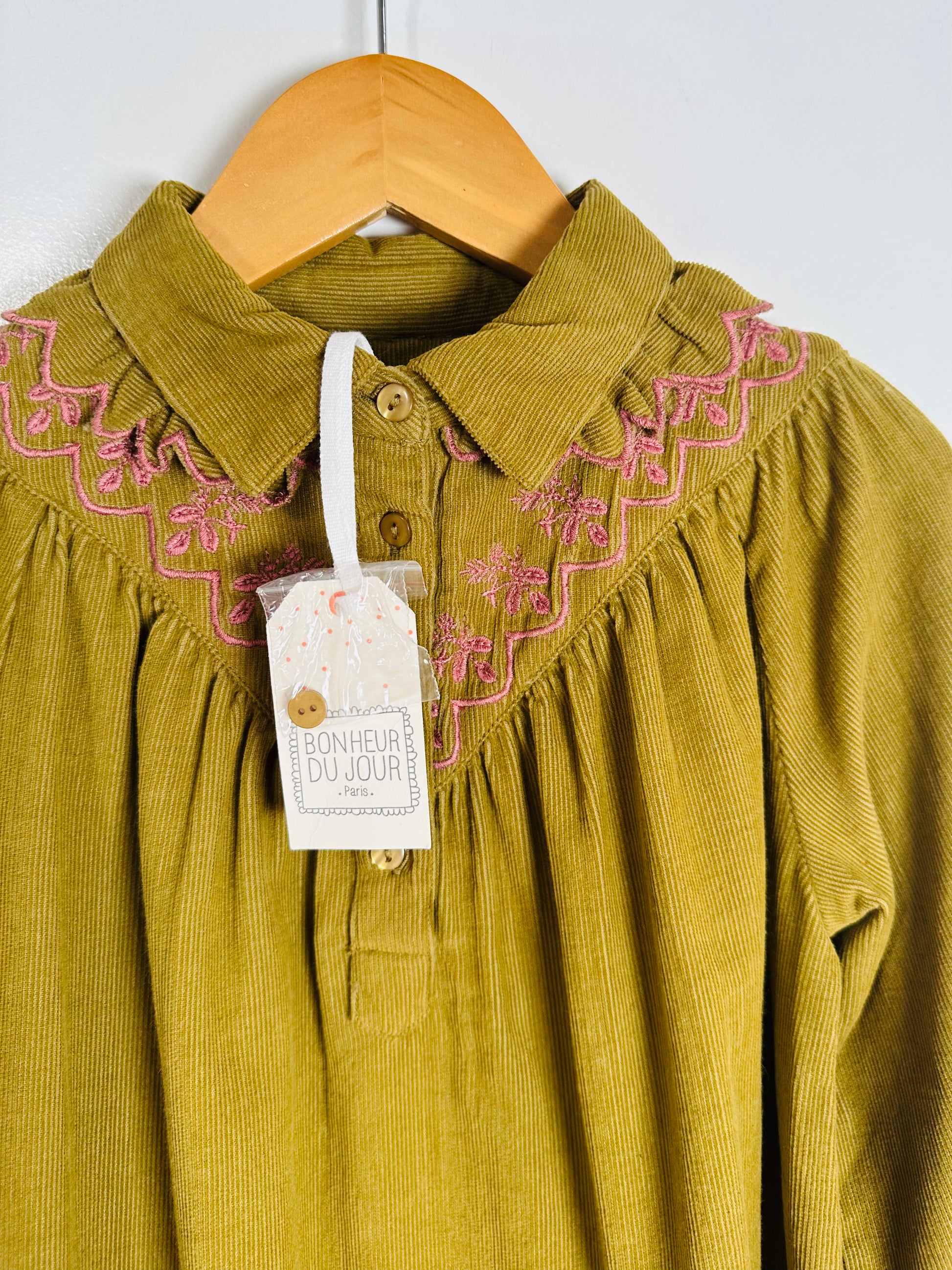 Green corduroy dress with pink embroidery on a hanger, featuring a brand tag.