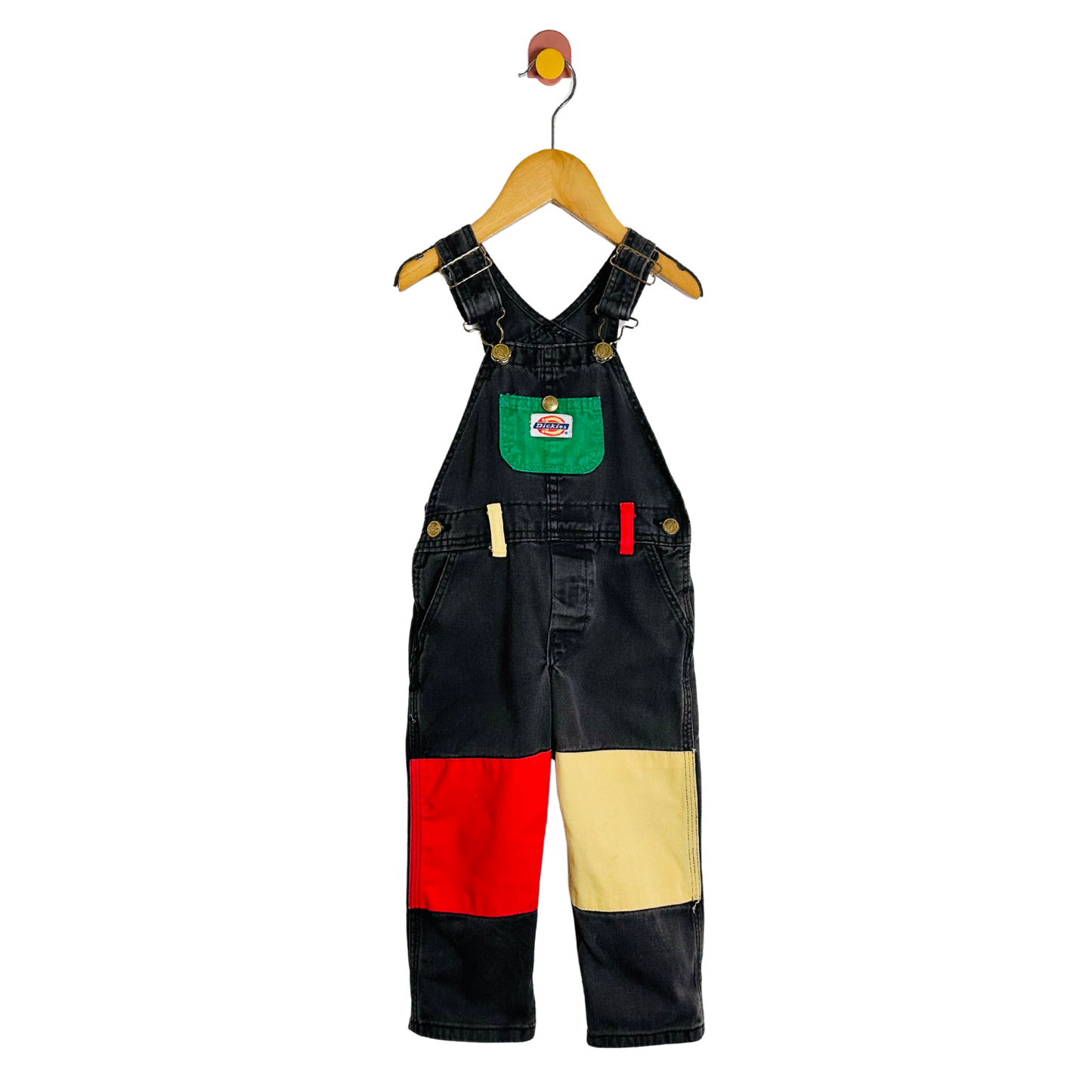 Black denim overalls with colorful patches on a hanger against a white background