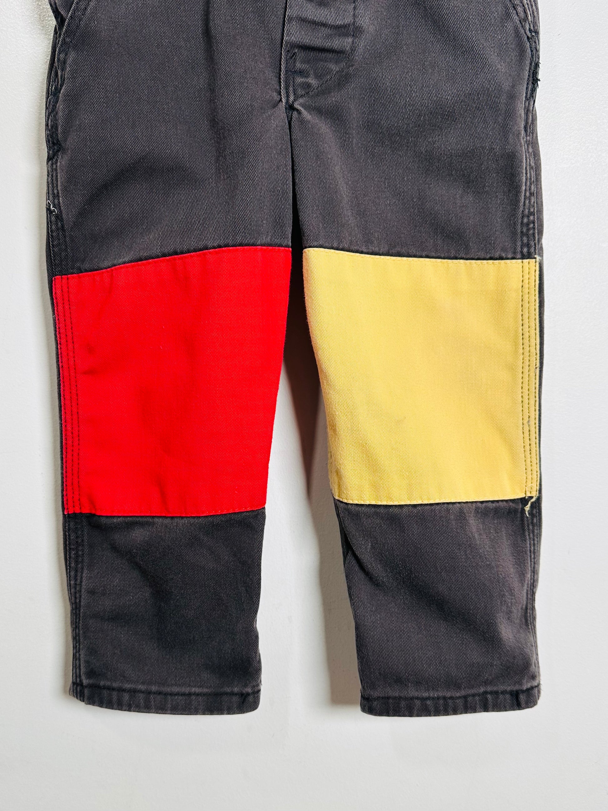 Color-blocked pants with red, yellow, and black sections on a light gray background