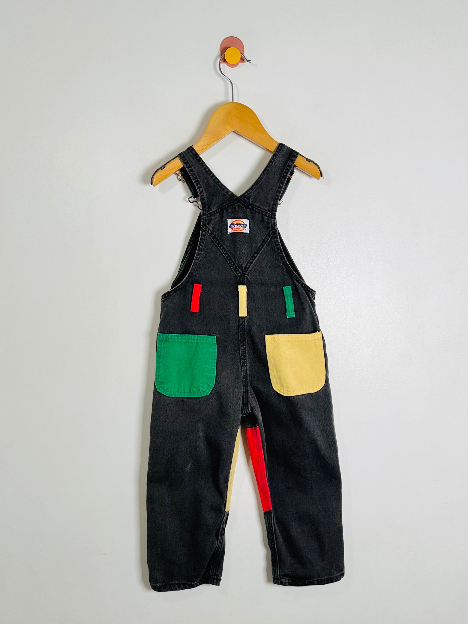 Black overalls with colorful patches on a hanger against a white background