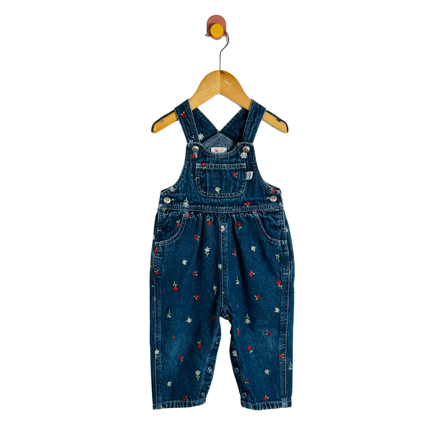 Blue denim overalls with floral patterns on a wooden hanger against a white background
