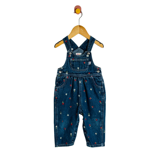 Blue denim overalls with floral patterns on a wooden hanger against a white background