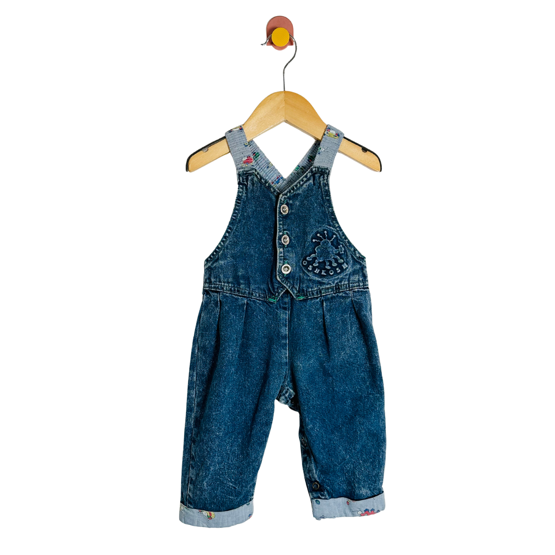 Blue denim overalls on a wooden hanger against a white background