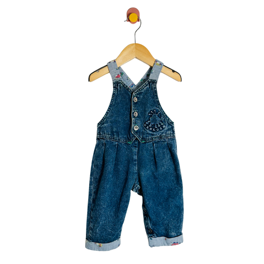Blue denim overalls on a wooden hanger against a white background