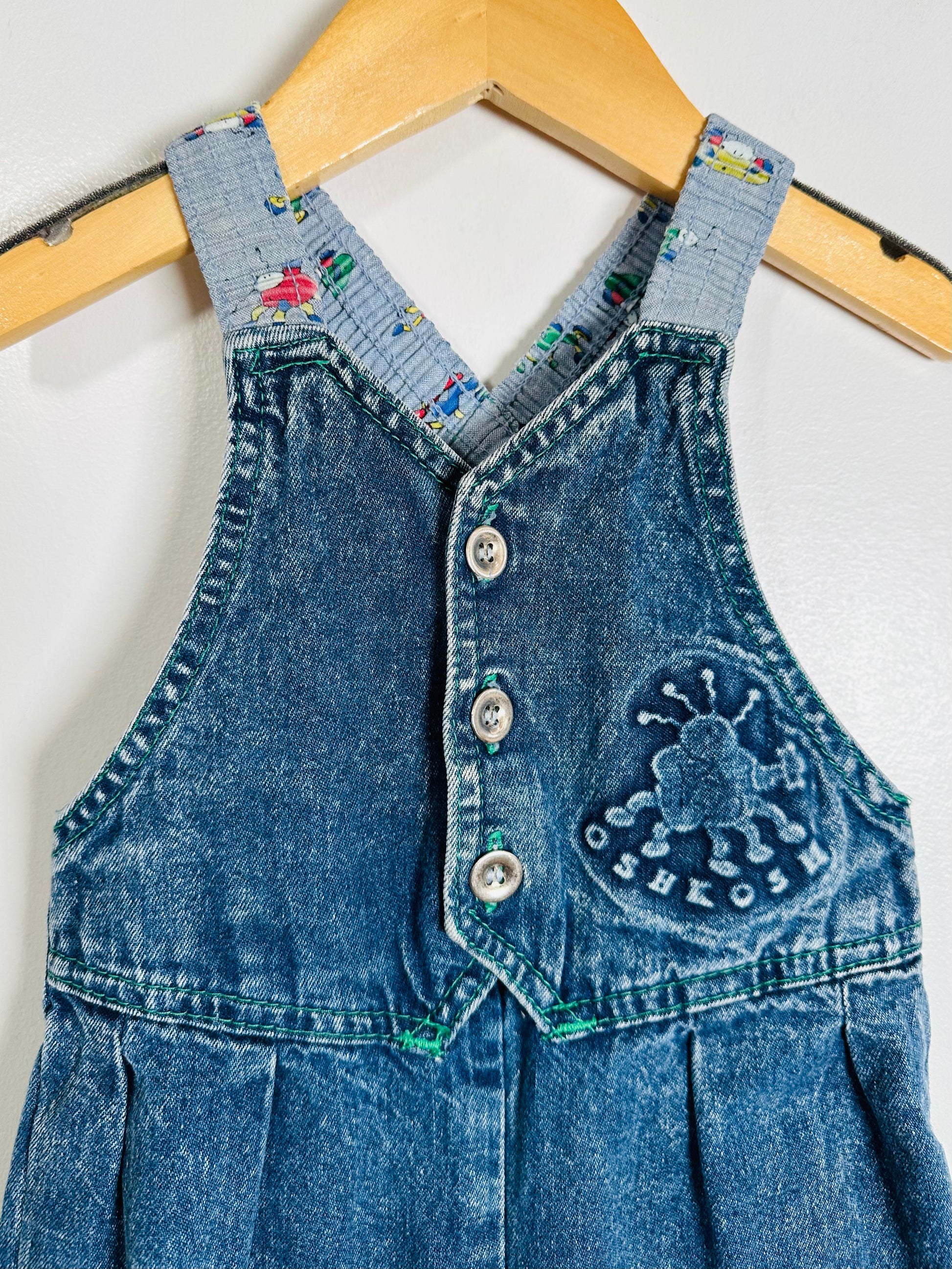 Blue denim overalls on a hanger against a white background