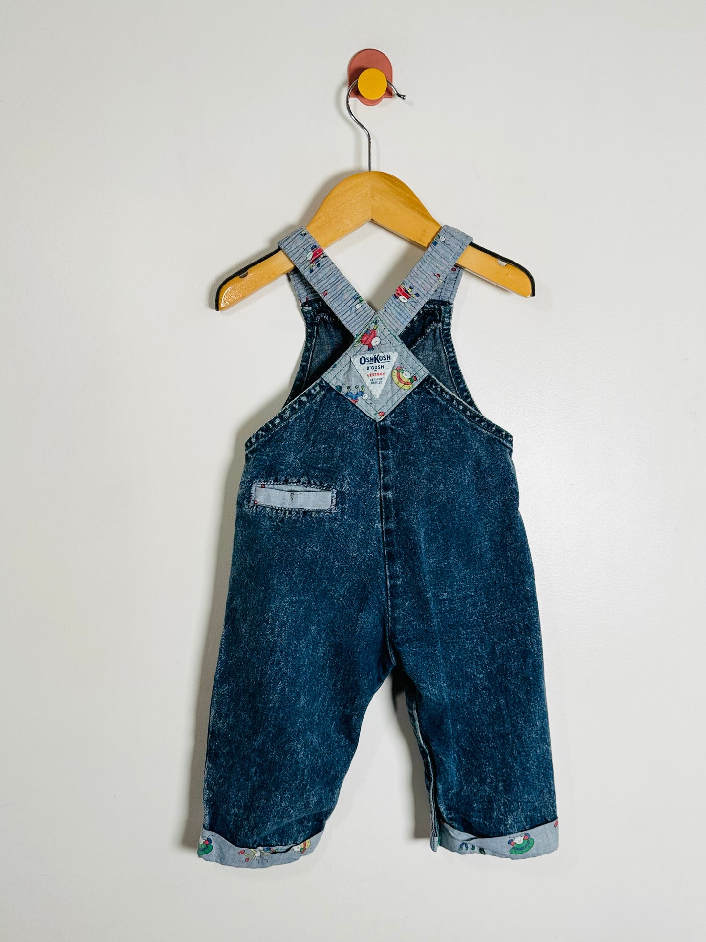 Blue denim overalls on a hanger against a white background