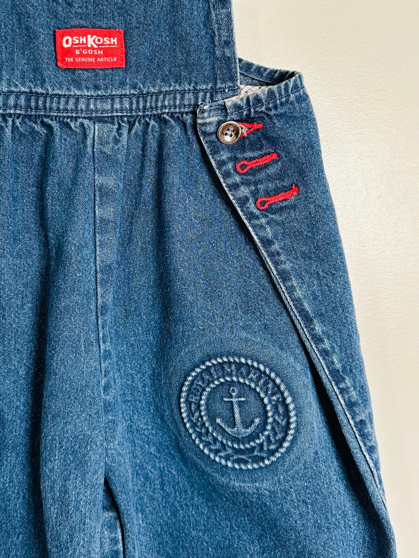 Blue denim apron with anchor emblem and Osh Kosh label on a beige background