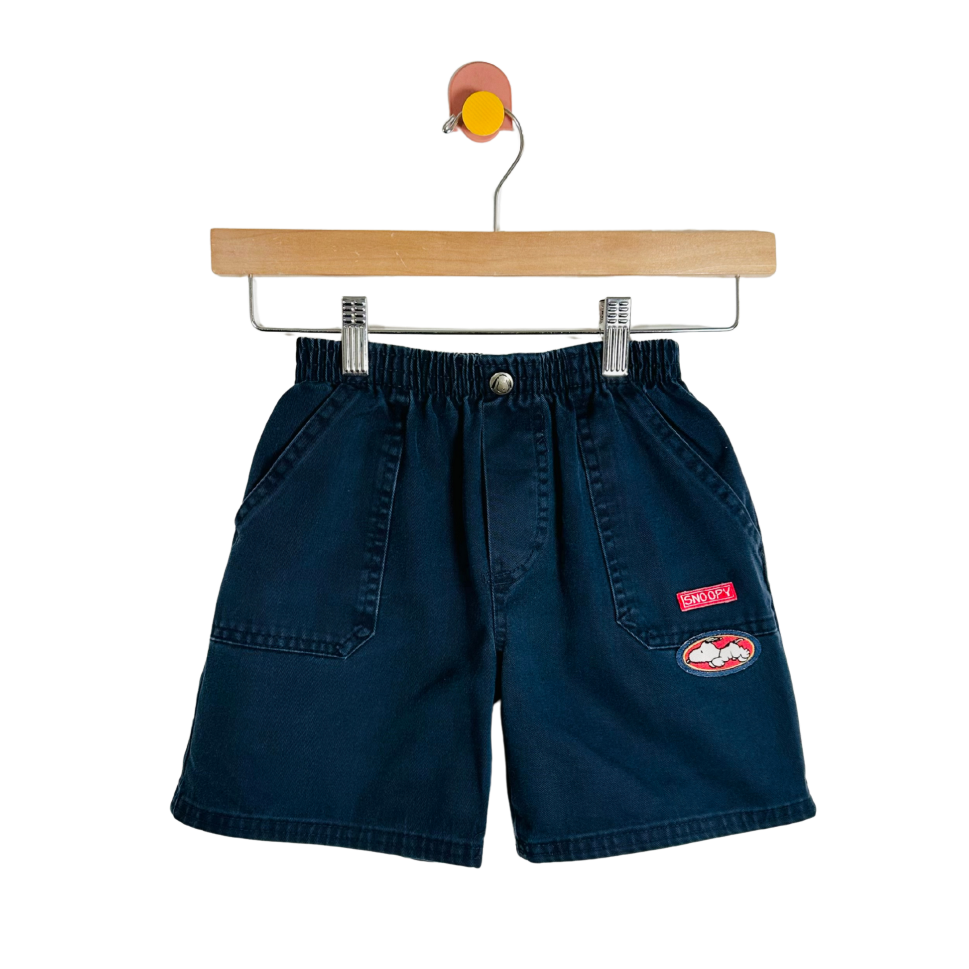 Navy blue shorts with a red patch on a wooden hanger against a white background