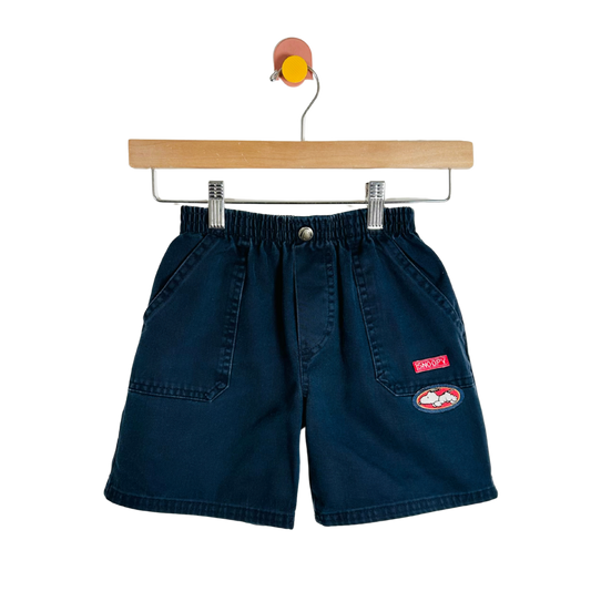 Navy blue shorts with a red patch on a wooden hanger against a white background