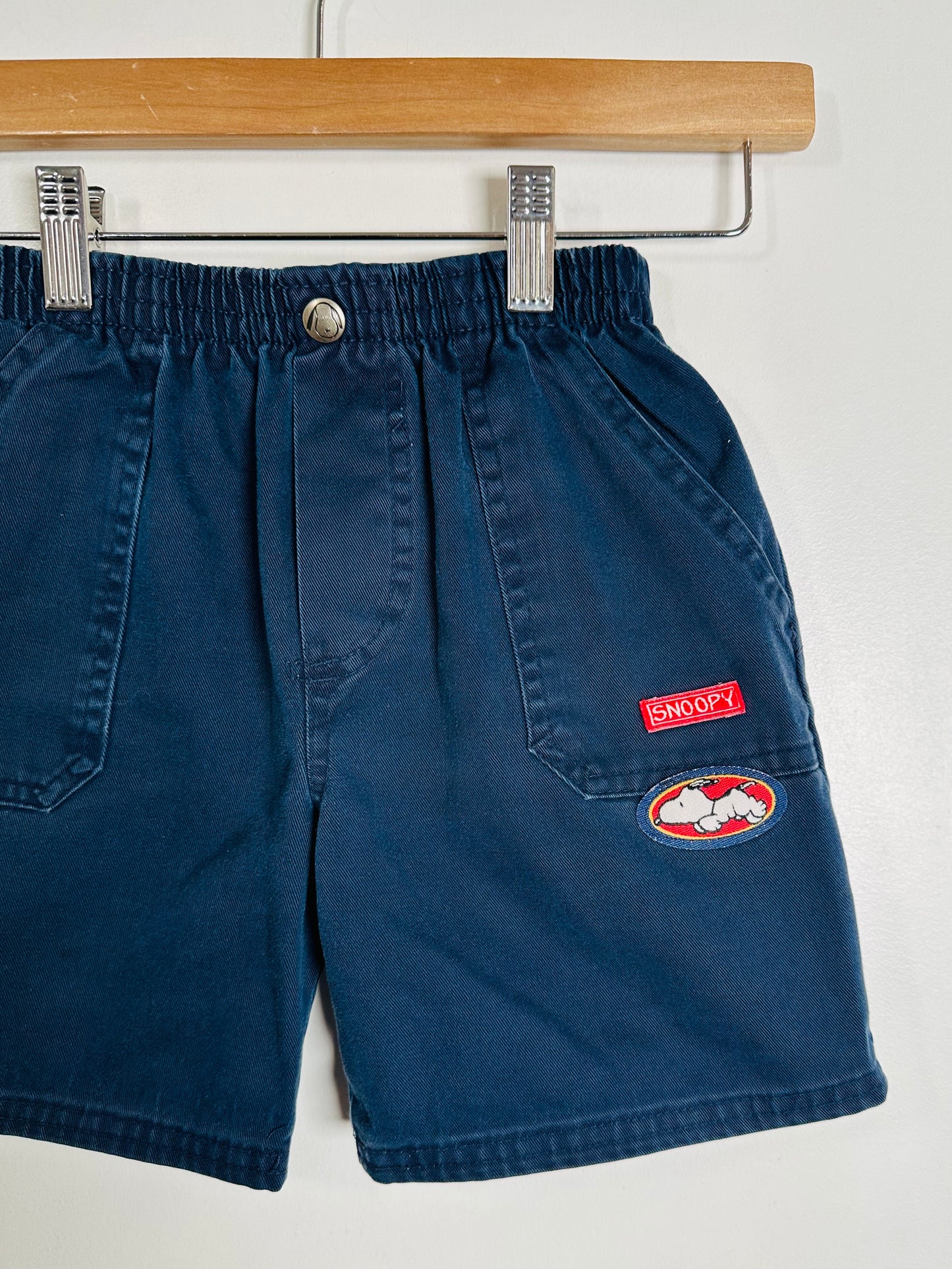 Blue shorts with patches on a hanger against a white background