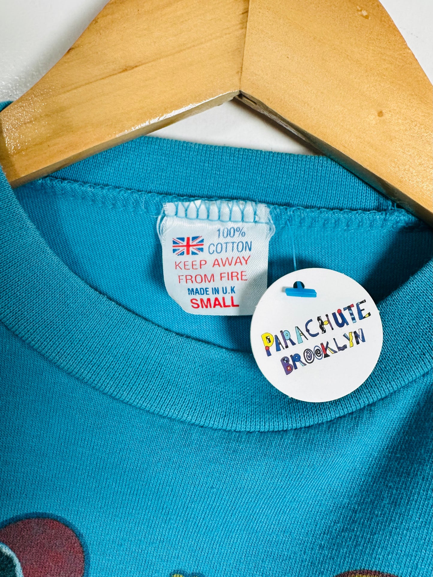 Close-up of a blue garment with a label and 'Parachute Brooklyn' tag on a wooden hanger.