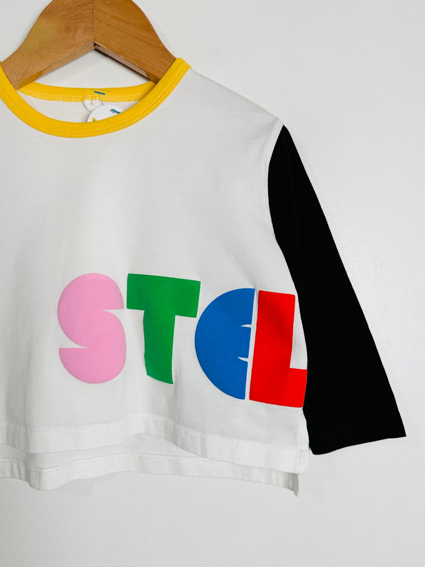 White crop top with colorful letters 'STEL' on a hanger against a white background