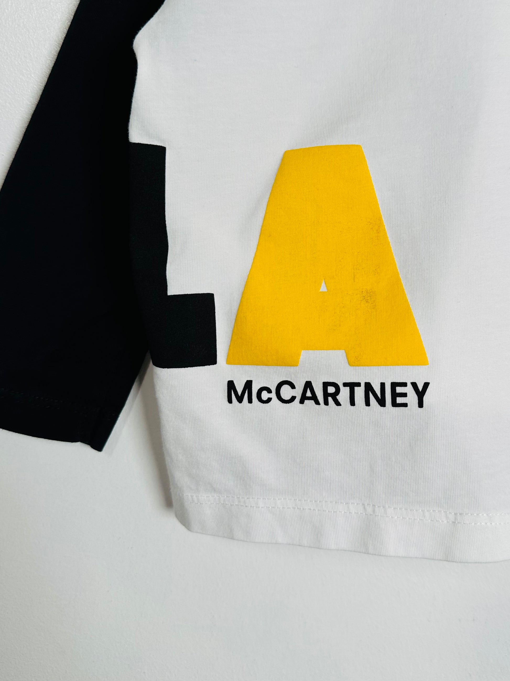 White shirt with a large yellow letter 'A' and the name 'McCartney' below it on a white background.