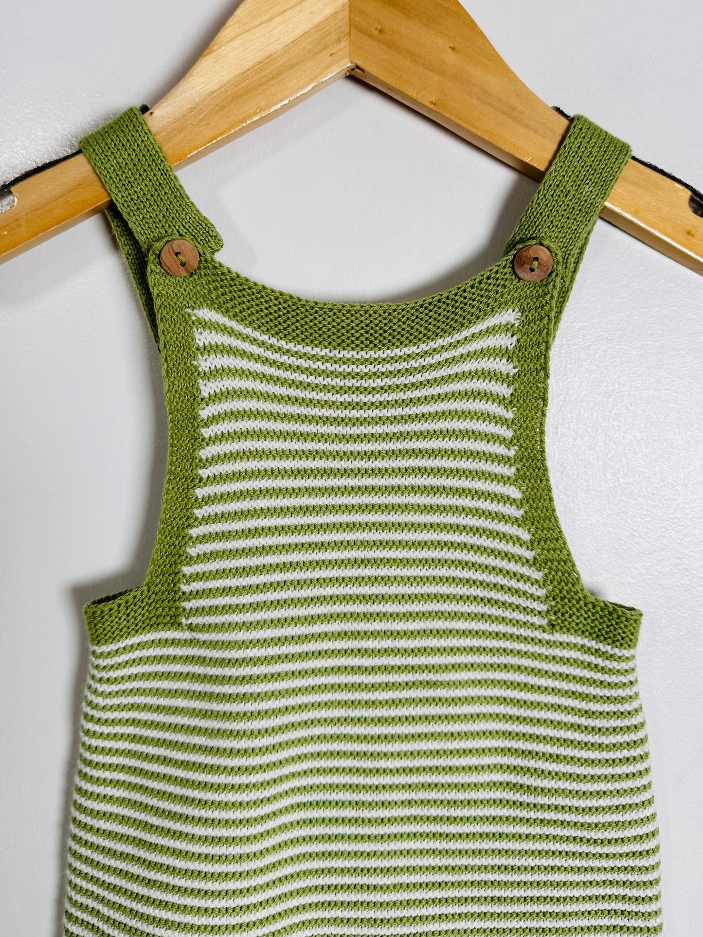 Green and white striped knitted romper on a wooden hanger against a white background