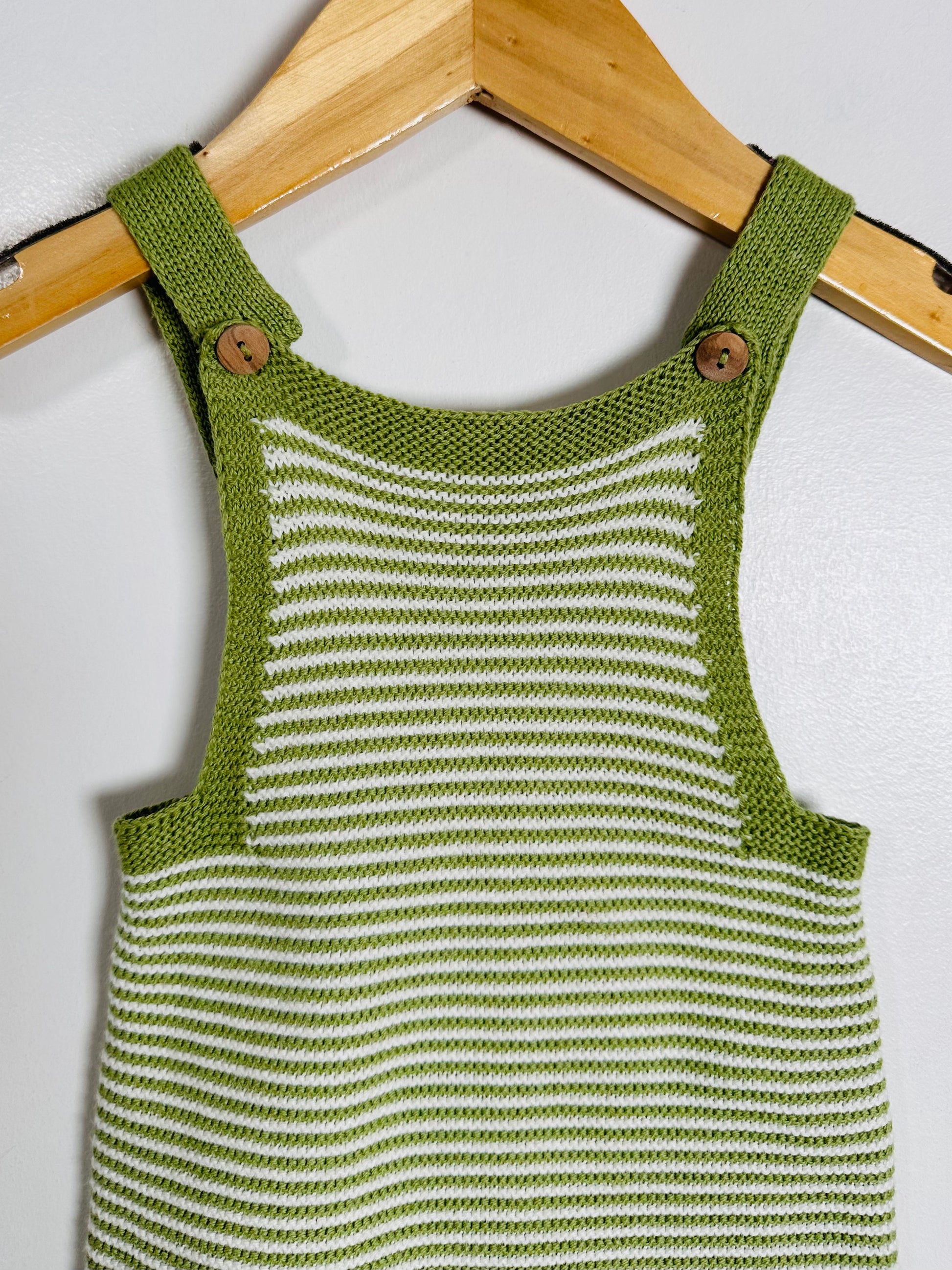 Green and white striped knitted romper on a wooden hanger against a white background