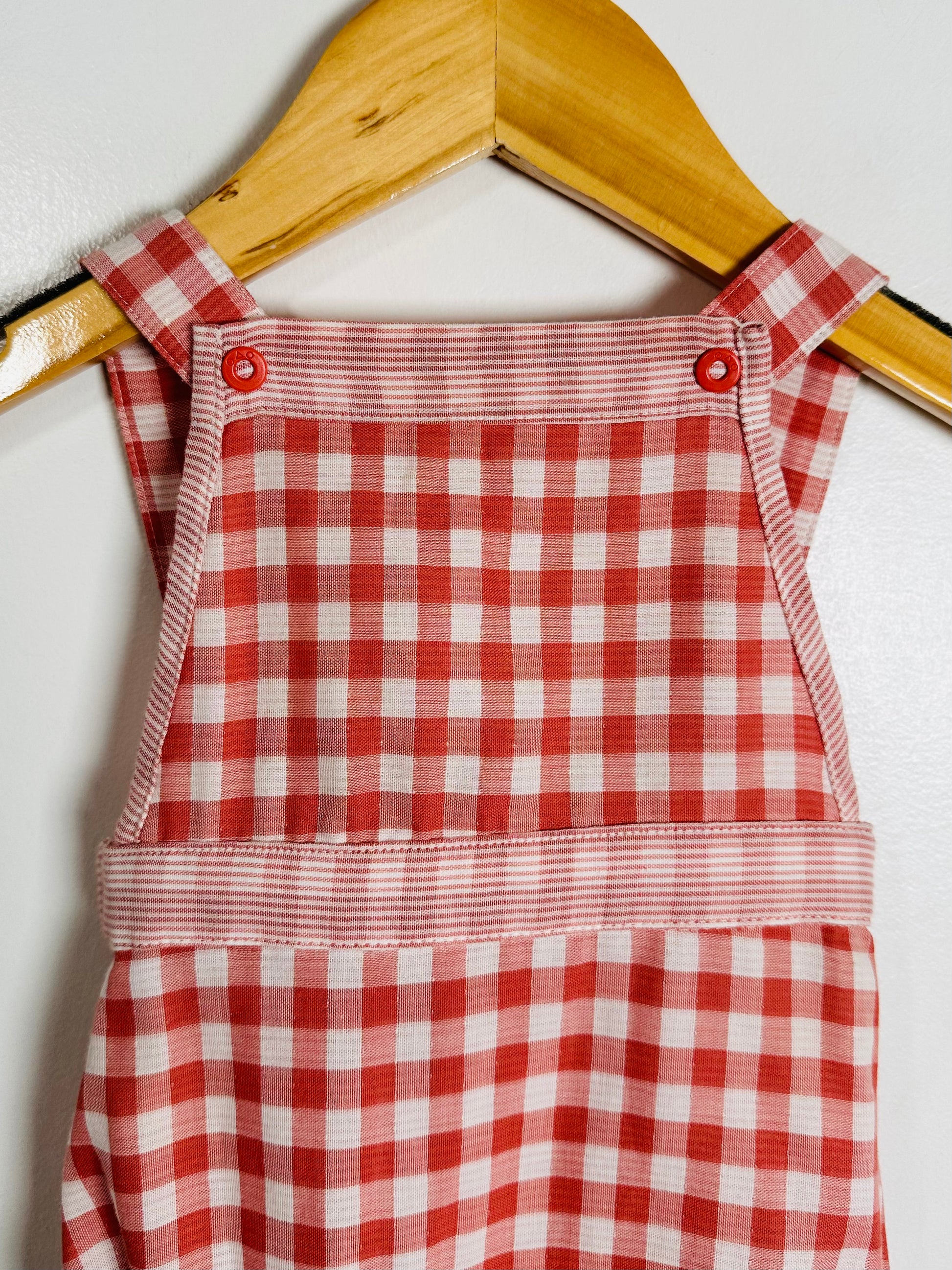 Red and white checkered dress on a wooden hanger against a white background