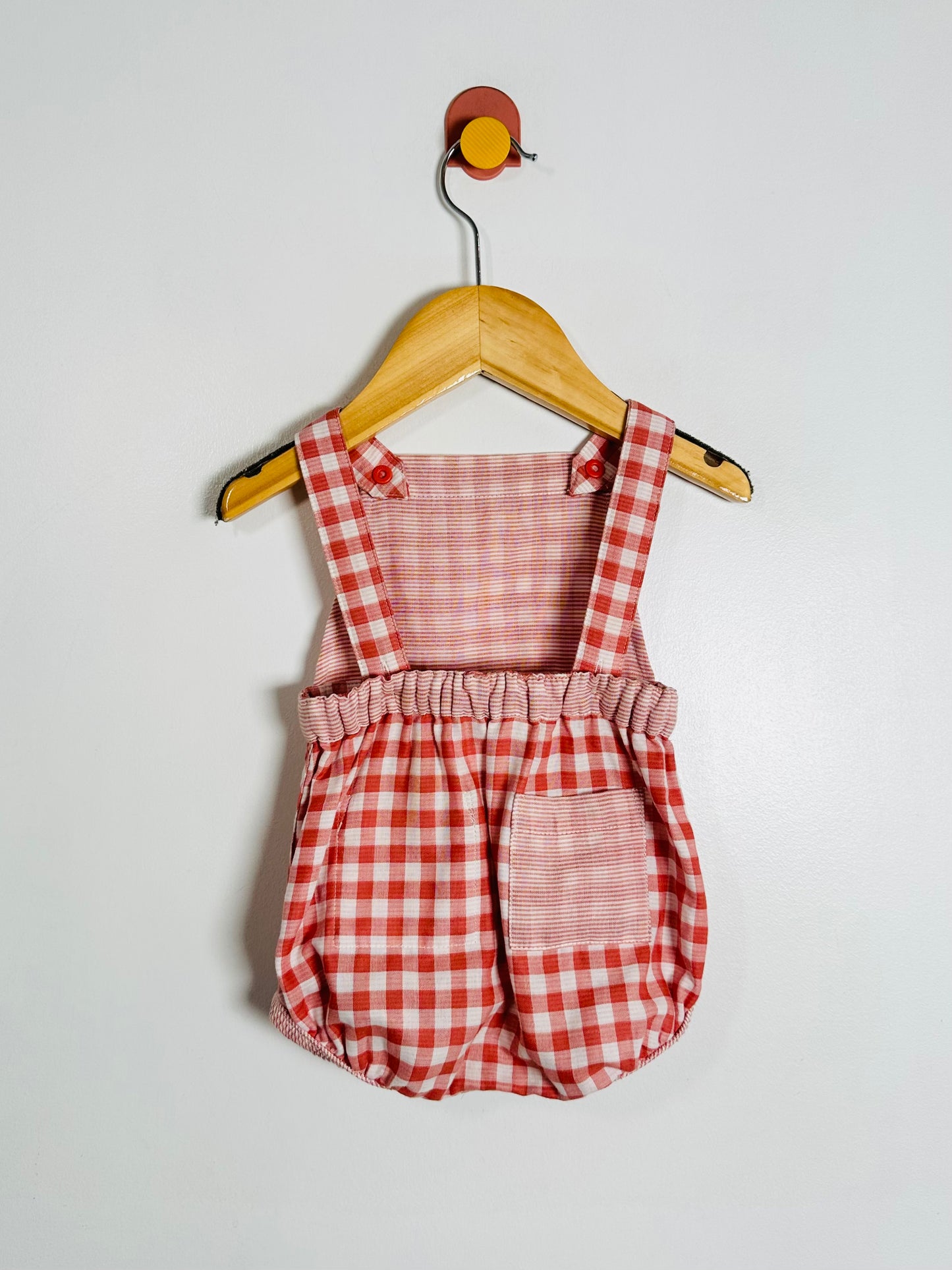 Red and white checkered romper on a wooden hanger against a white background