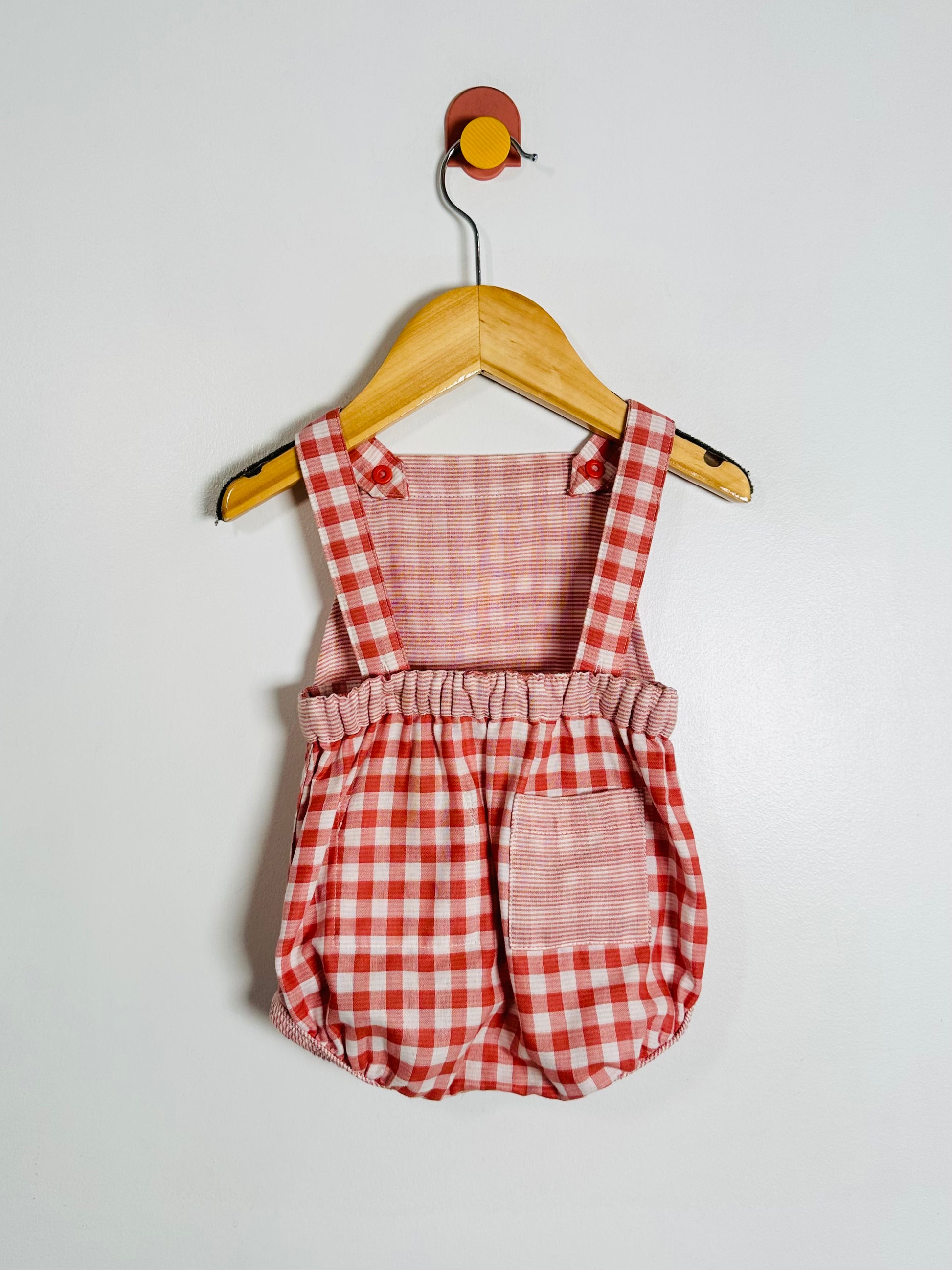 Red and white checkered romper on a wooden hanger against a white background