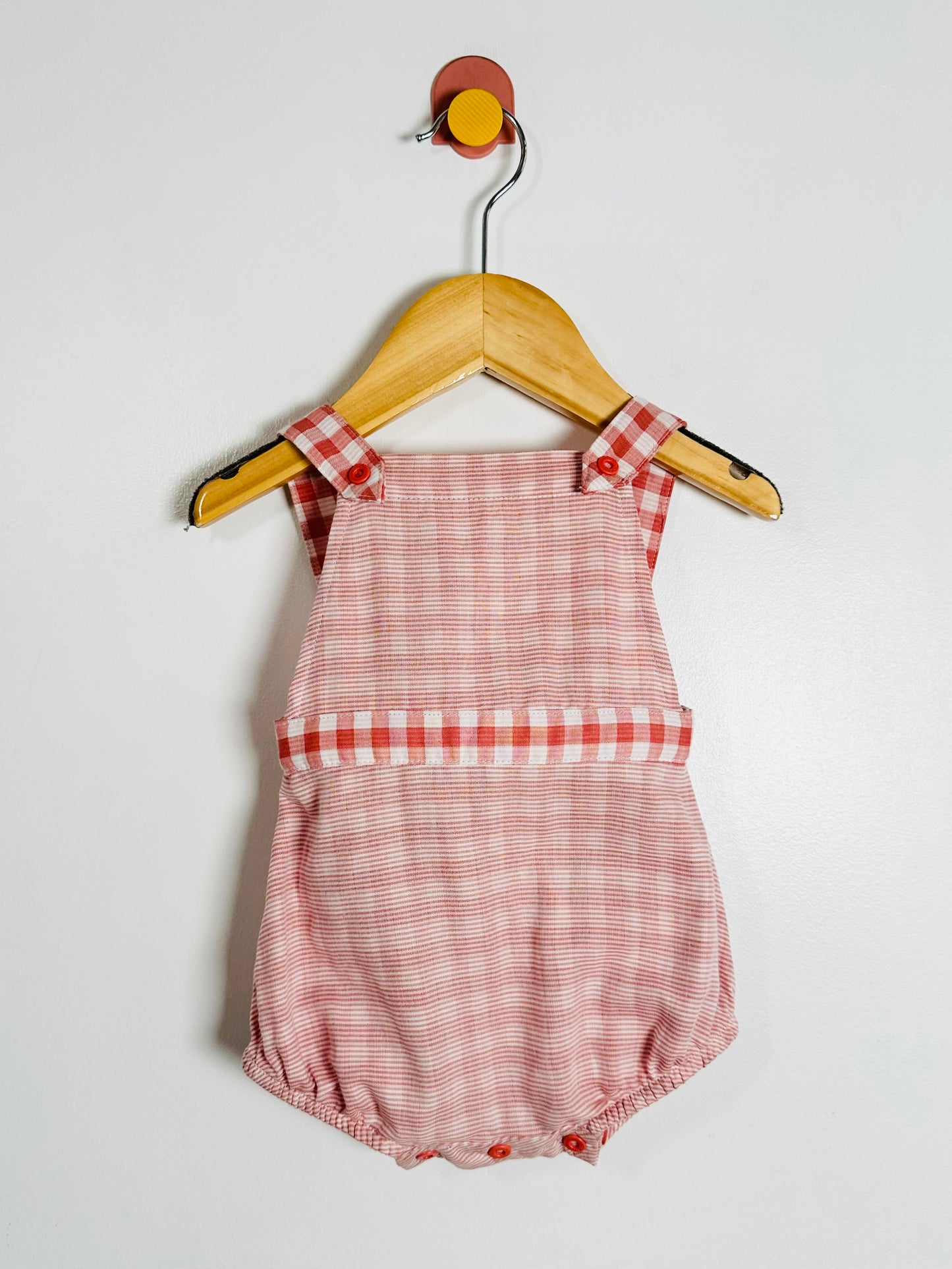 red checkered romper on a wooden hanger against a white background