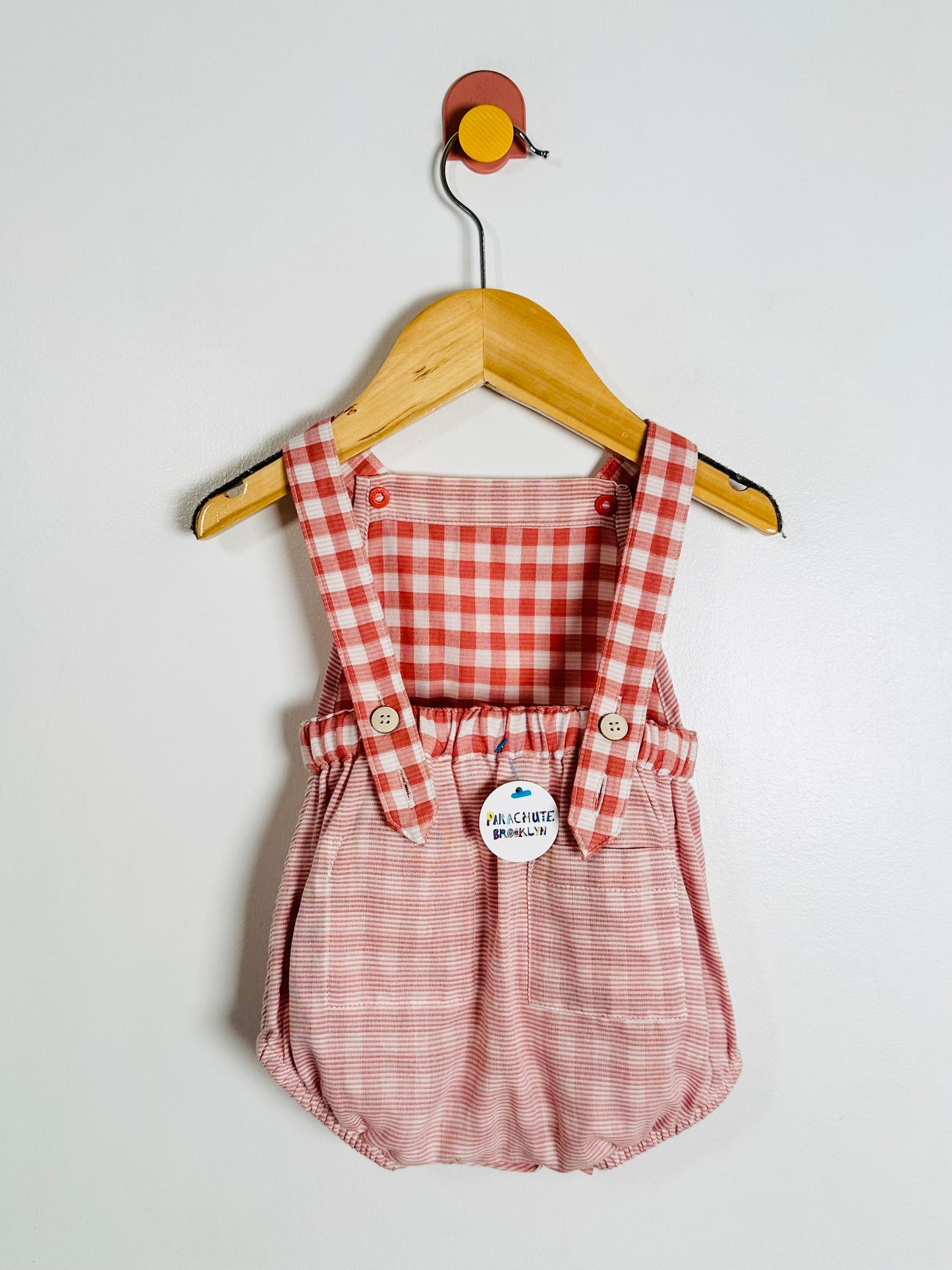 Red and white checkered romper with suspenders on a hanger against a light gray background