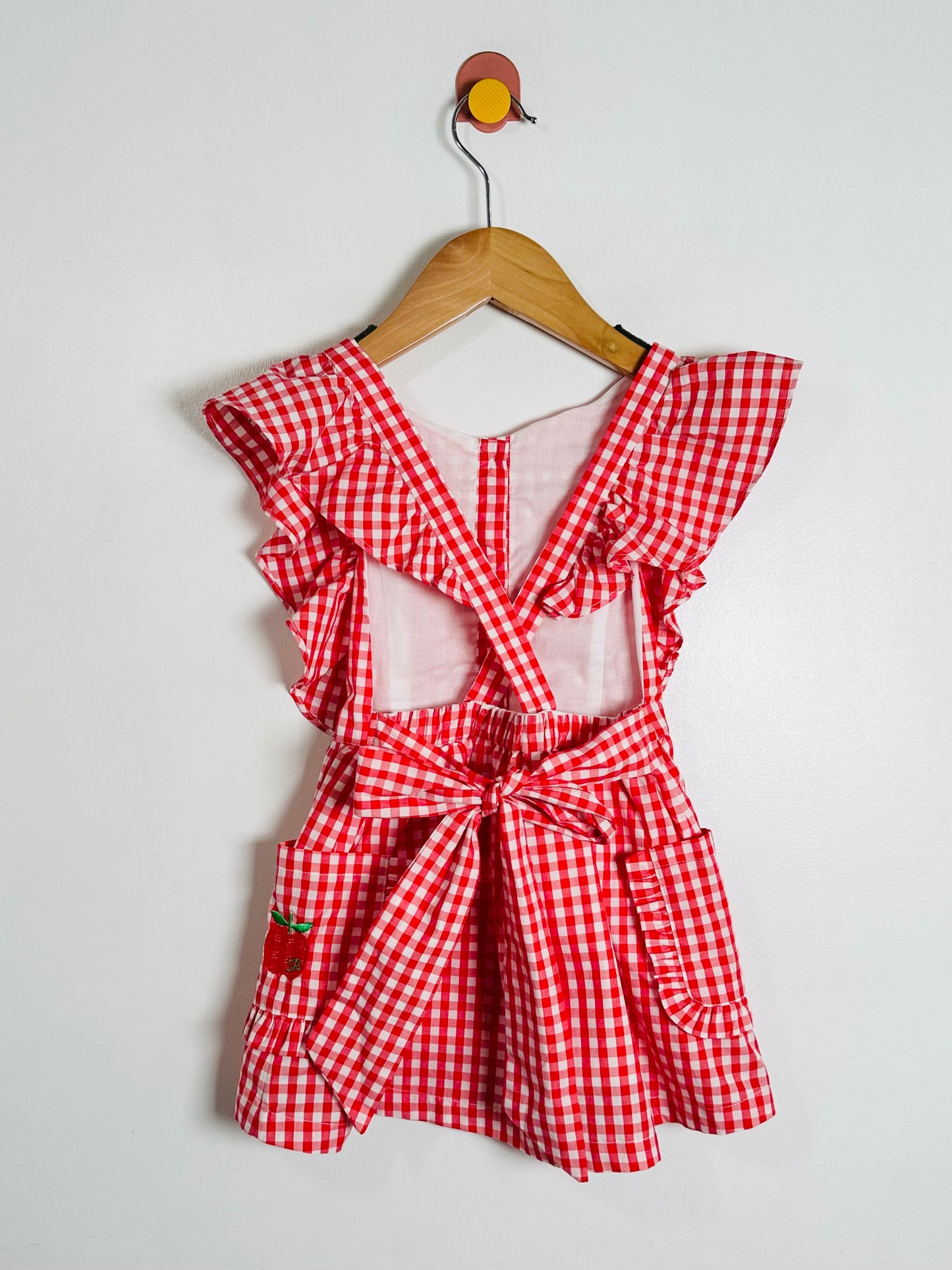 Red and white checkered dress with ruffled sleeves on a hanger against a white background