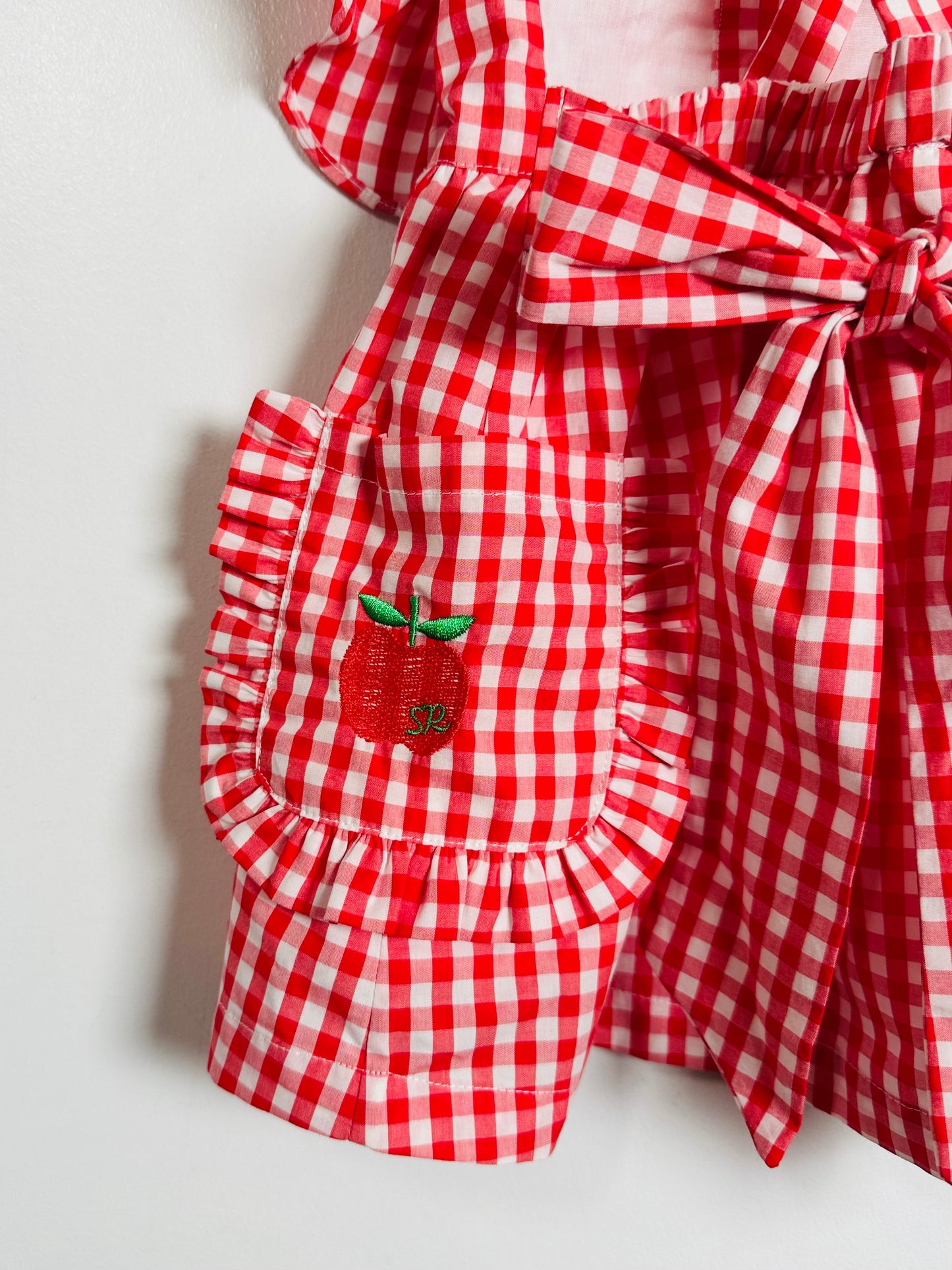 Red and white checkered apron with a embroidered apple on a light background