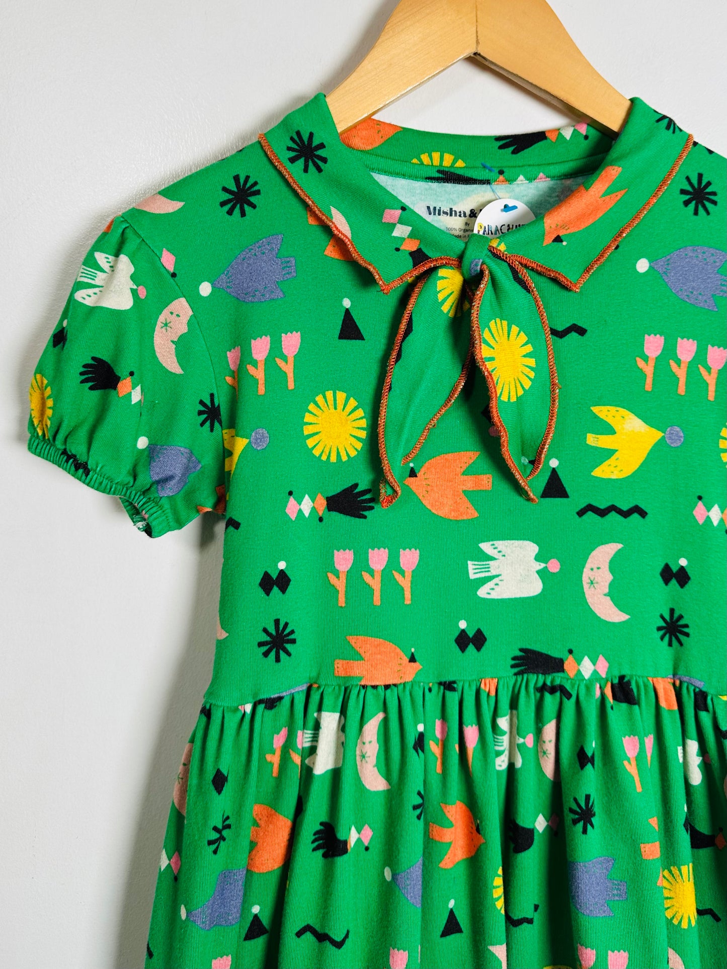 Green dress with colorful pattern on a hanger against a white background