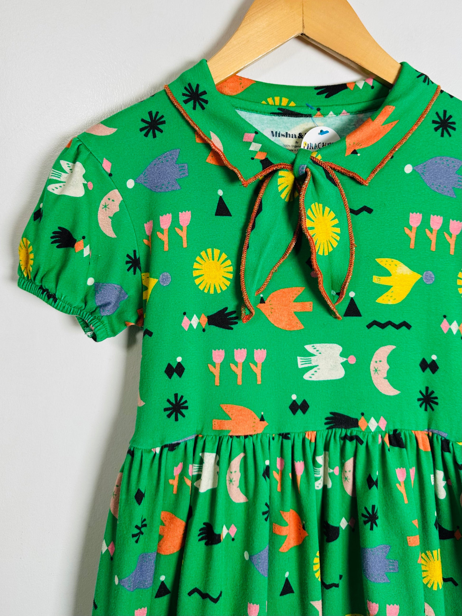 Green dress with colorful pattern on a hanger against a white background