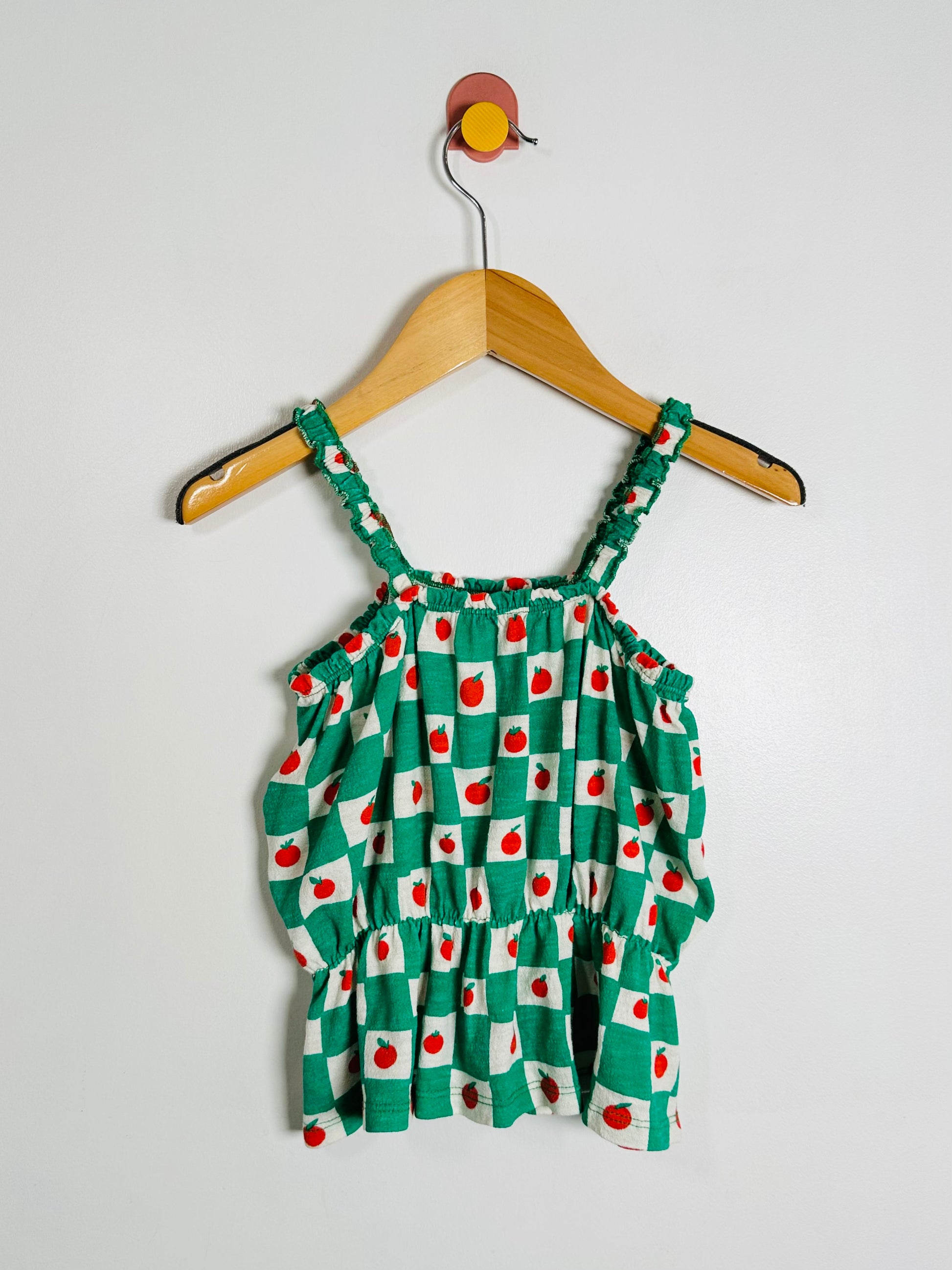 Green checkered dress with red cherries on a hanger against a white background