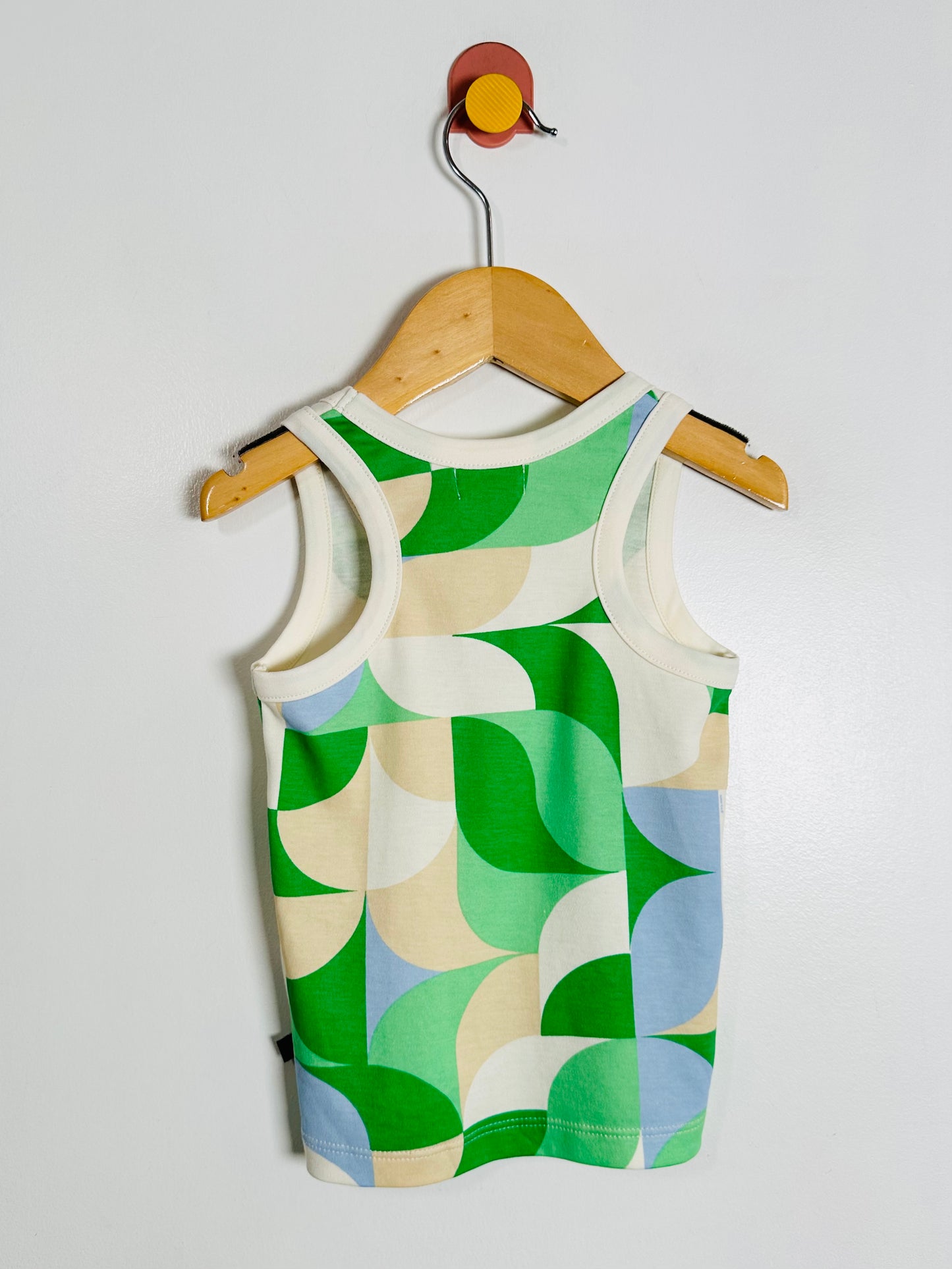 Children's tank top with green and beige pattern on a wooden hanger against a white background