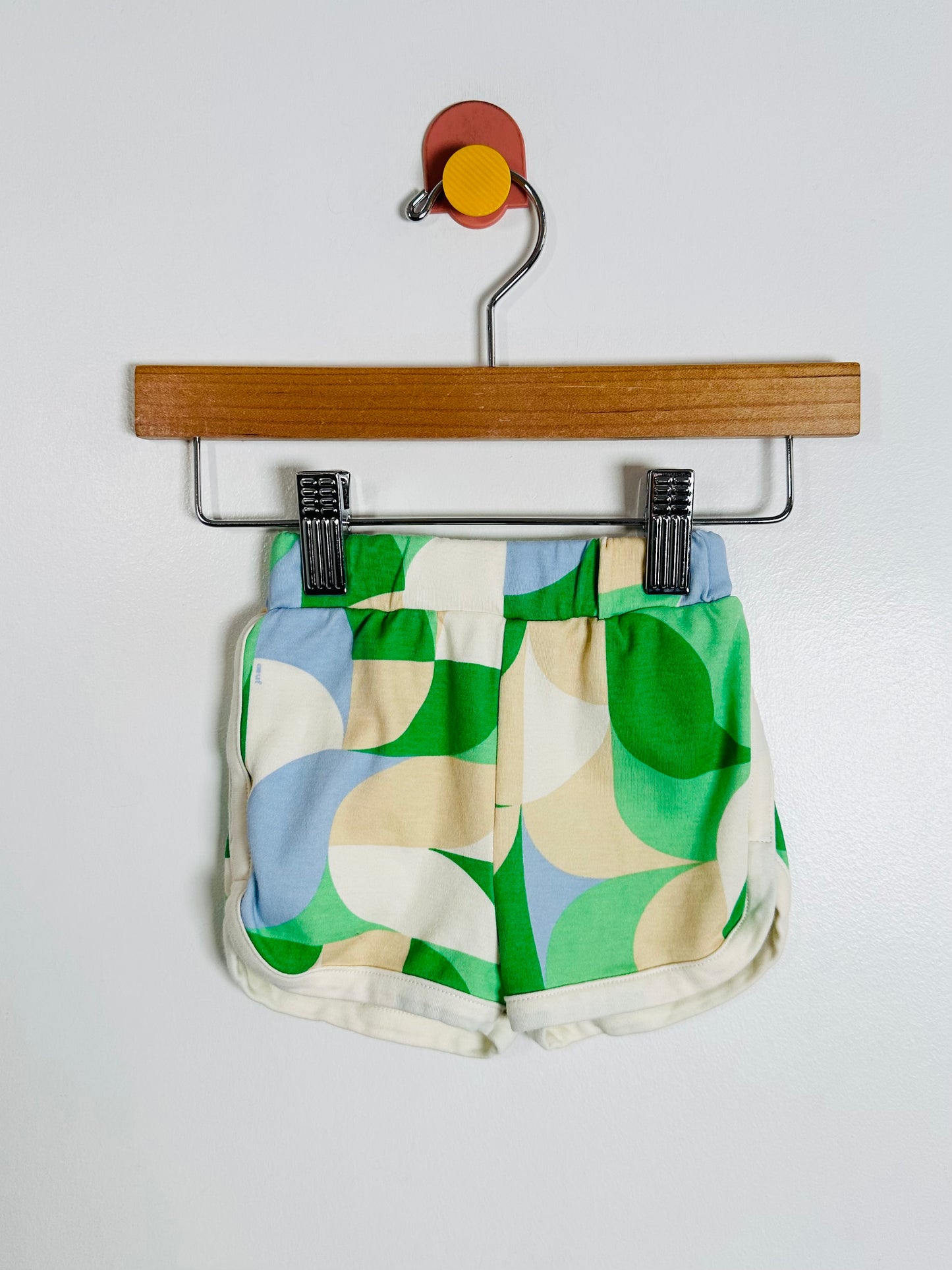 Green and beige patterned shorts on a hanger against a white background