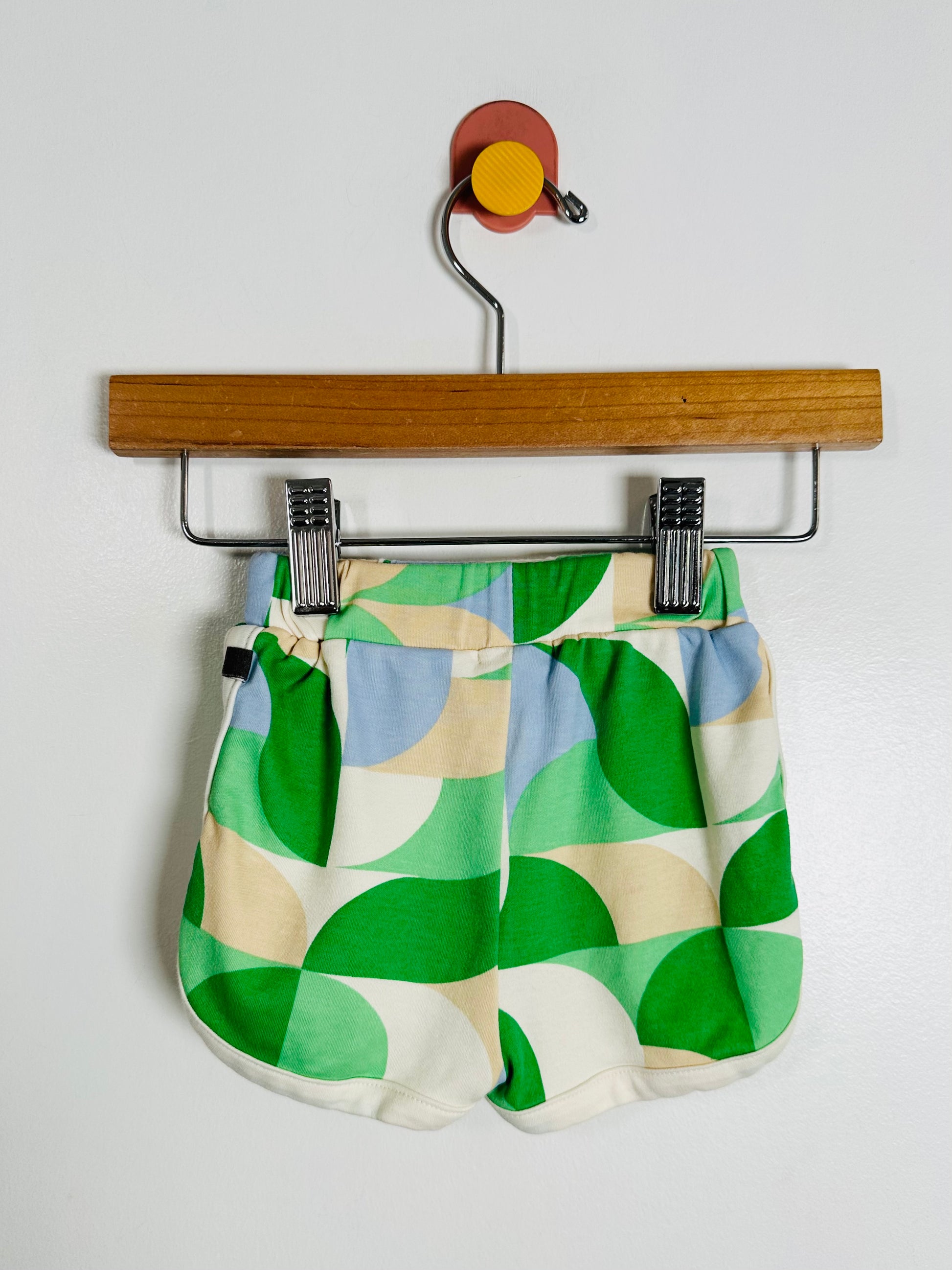 Colorful geometric-patterned shorts on a wooden hanger against a white background