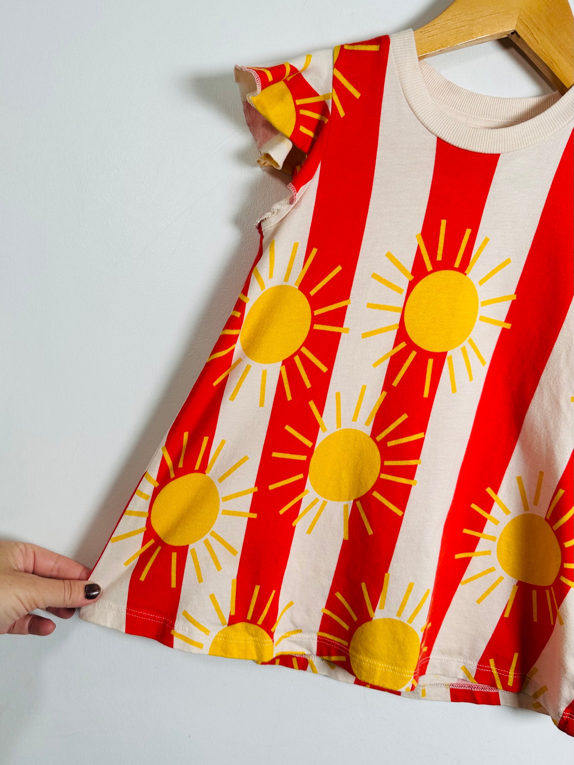 Children's dress with sun pattern on a hanger against a white background
