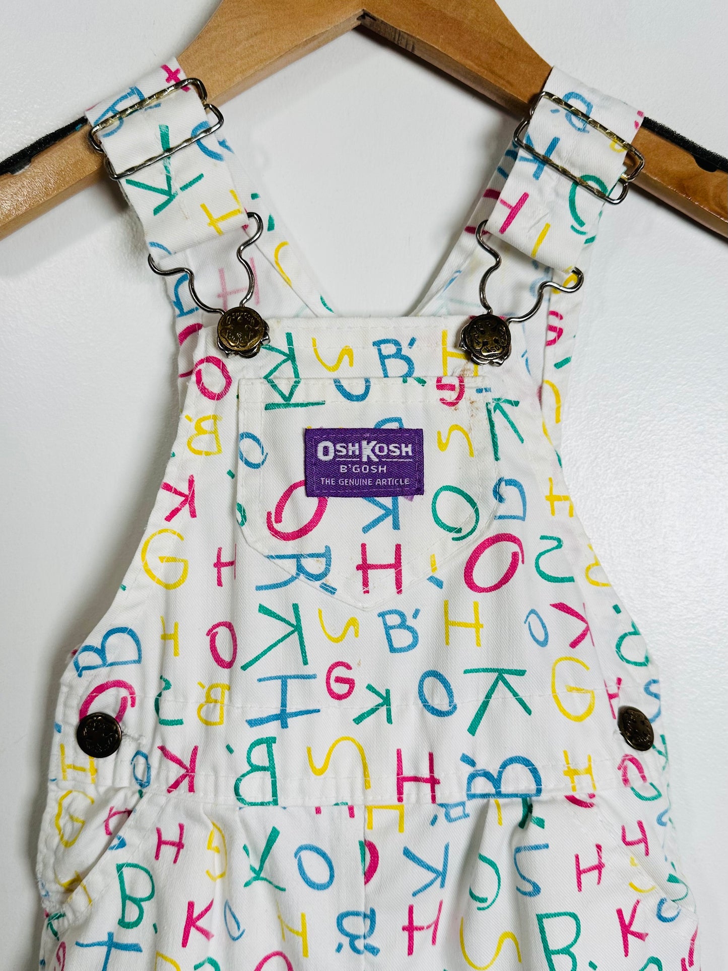 Children's overalls with colorful letter pattern and OshKosh logo on a white background
