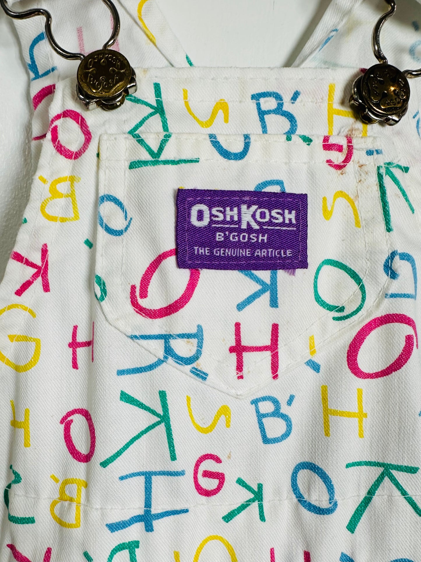 Children's overalls with colorful letter pattern and OshKosh logo.