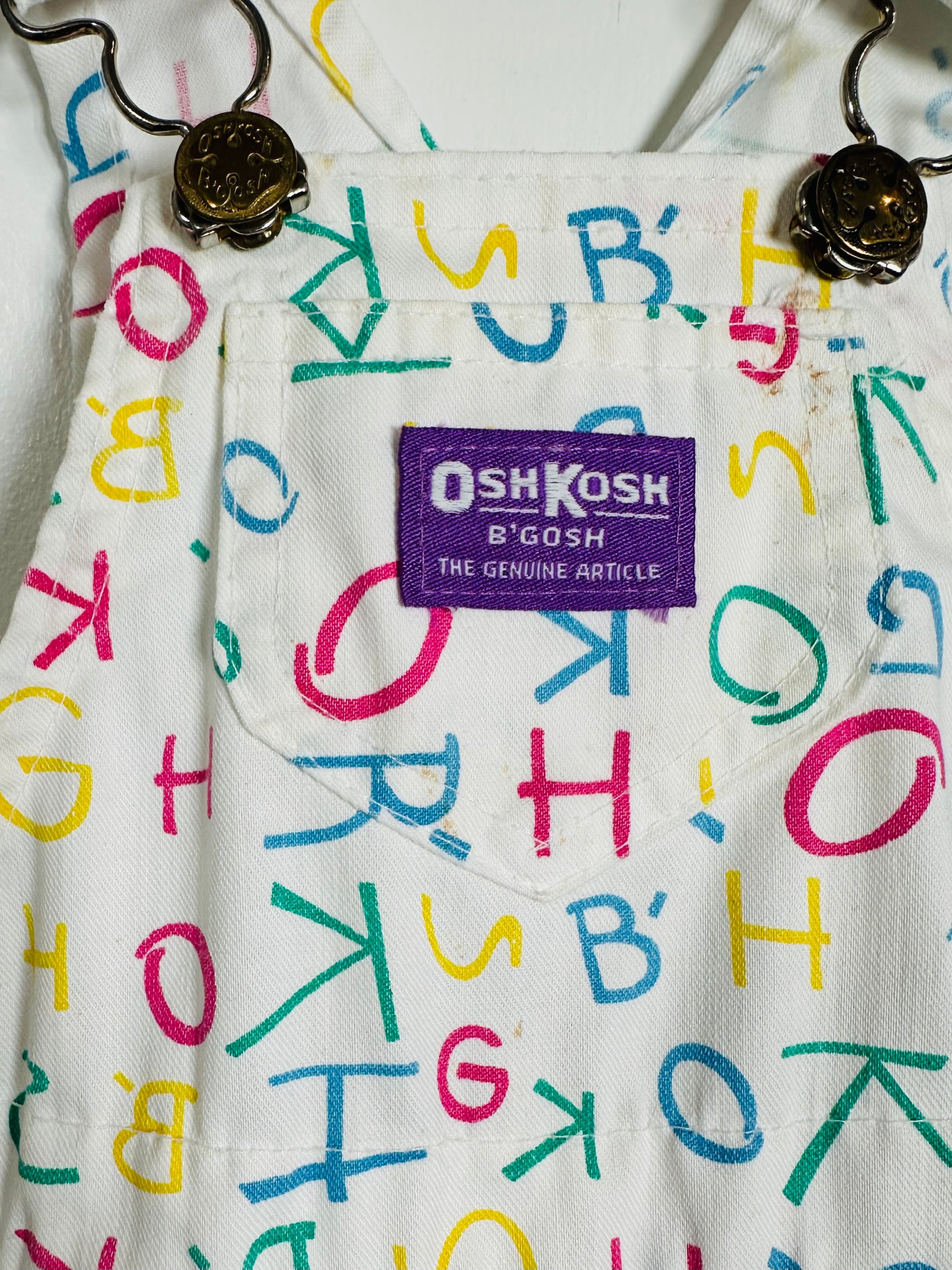 Children's overalls with colorful letter pattern and OshKosh logo.