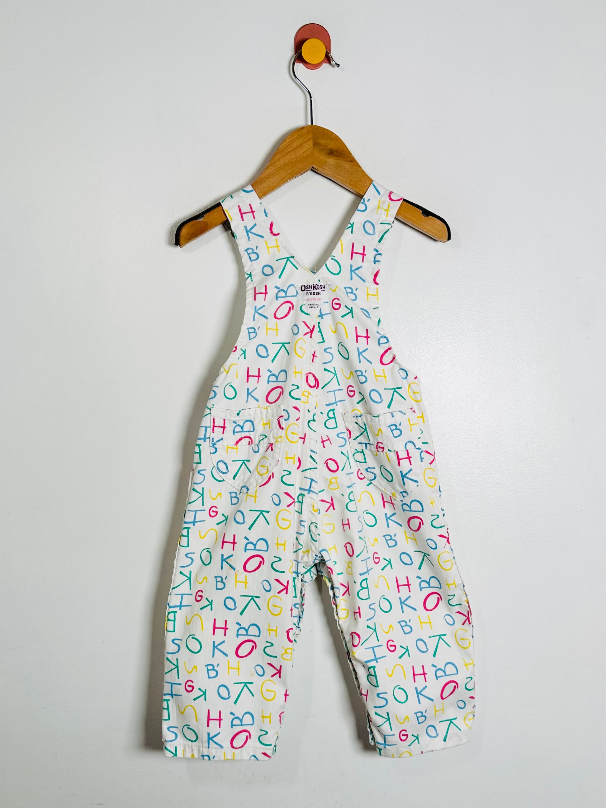 Children's overalls with colorful letter pattern on a hanger against a white background