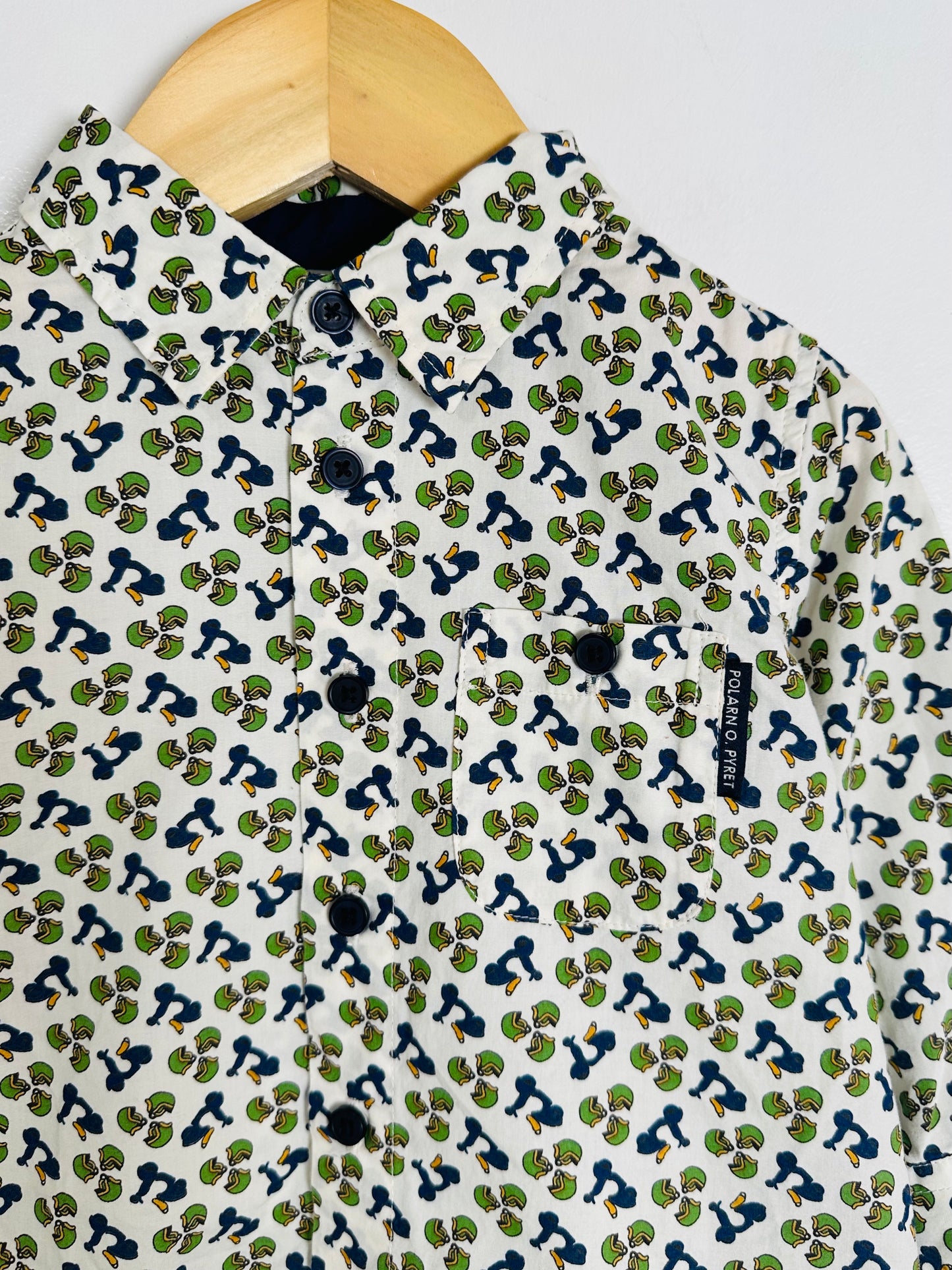 Patterned shirt with small designs on a hanger against a light background
