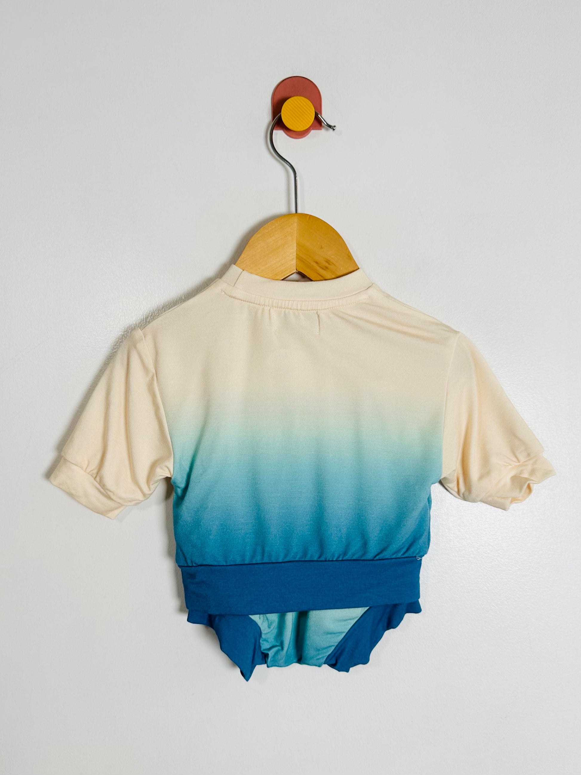 Gradient baby outfit with a white top and blue bottom on a hanger against a light gray background