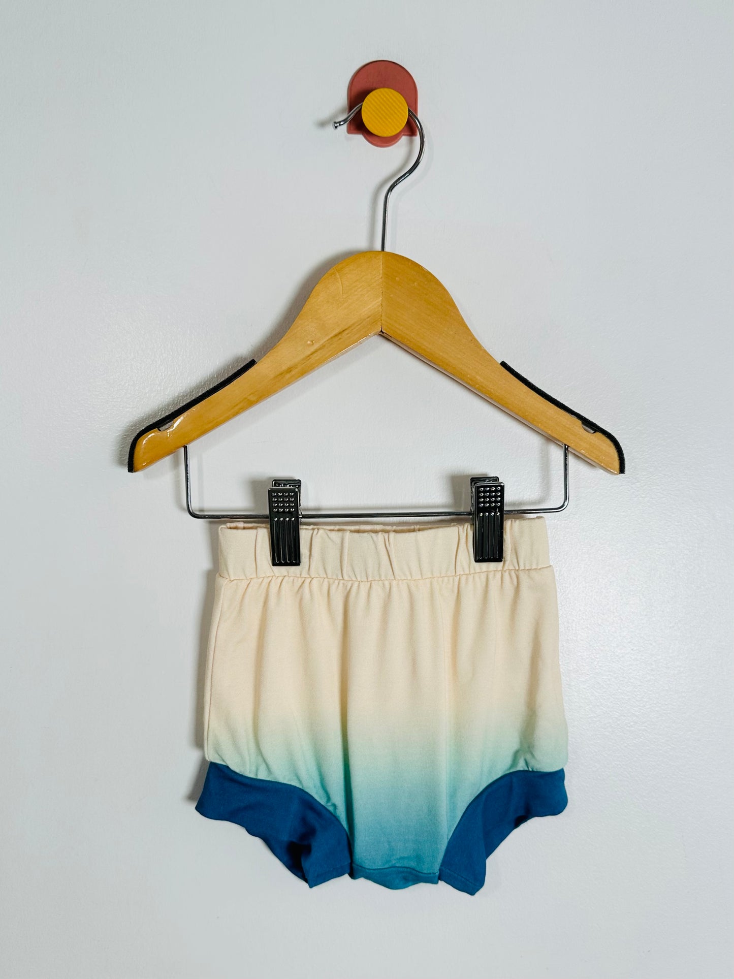 Ombre shorts with blue to beige gradient on a hanger against a white background