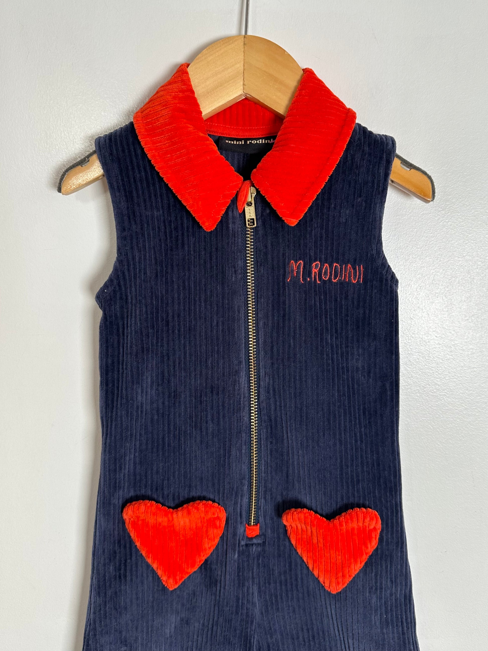 Navy blue corduroy vest with red heart details and collar on a hanger