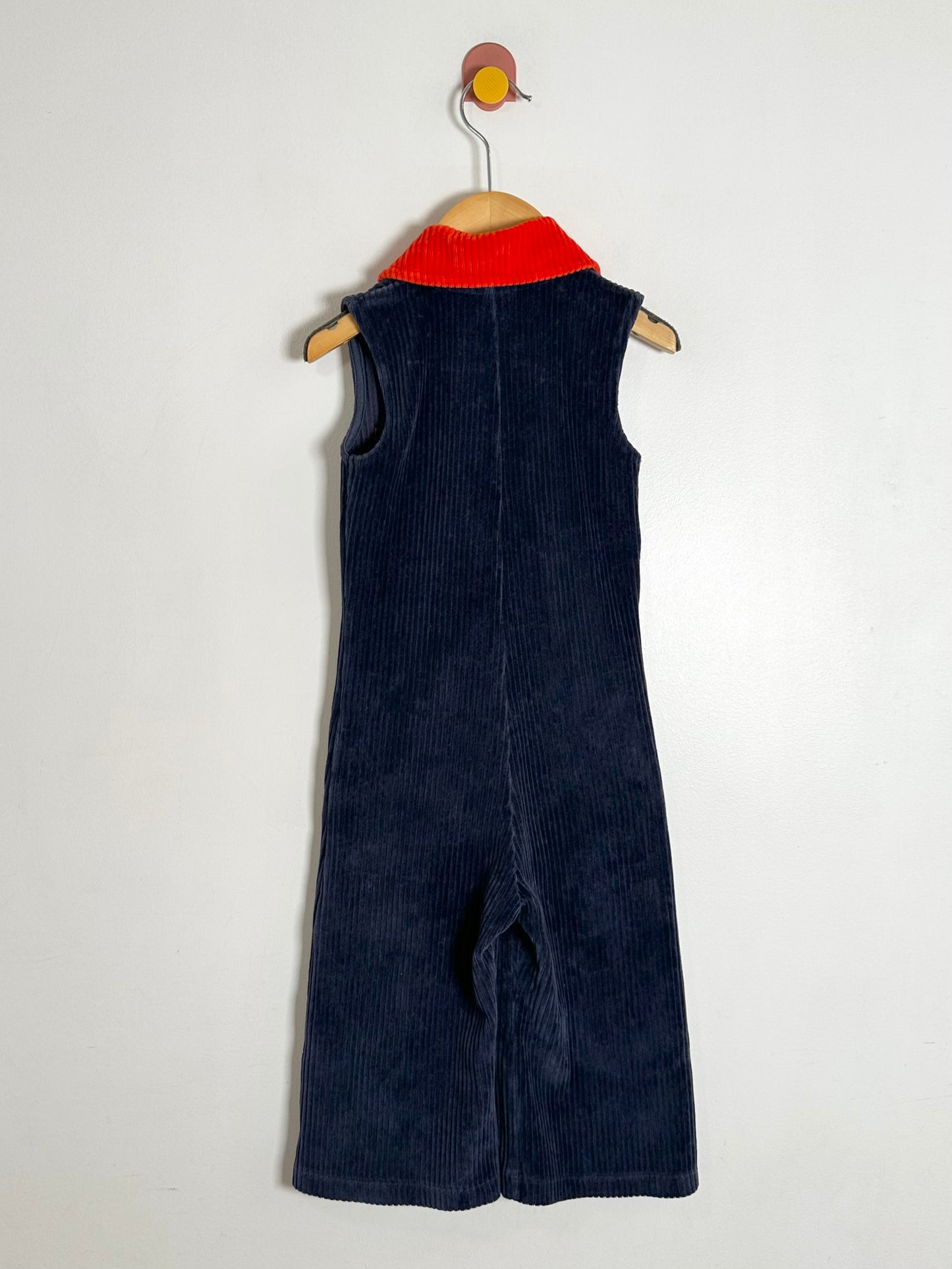 Navy blue corduroy jumpsuit on a hanger against a white background